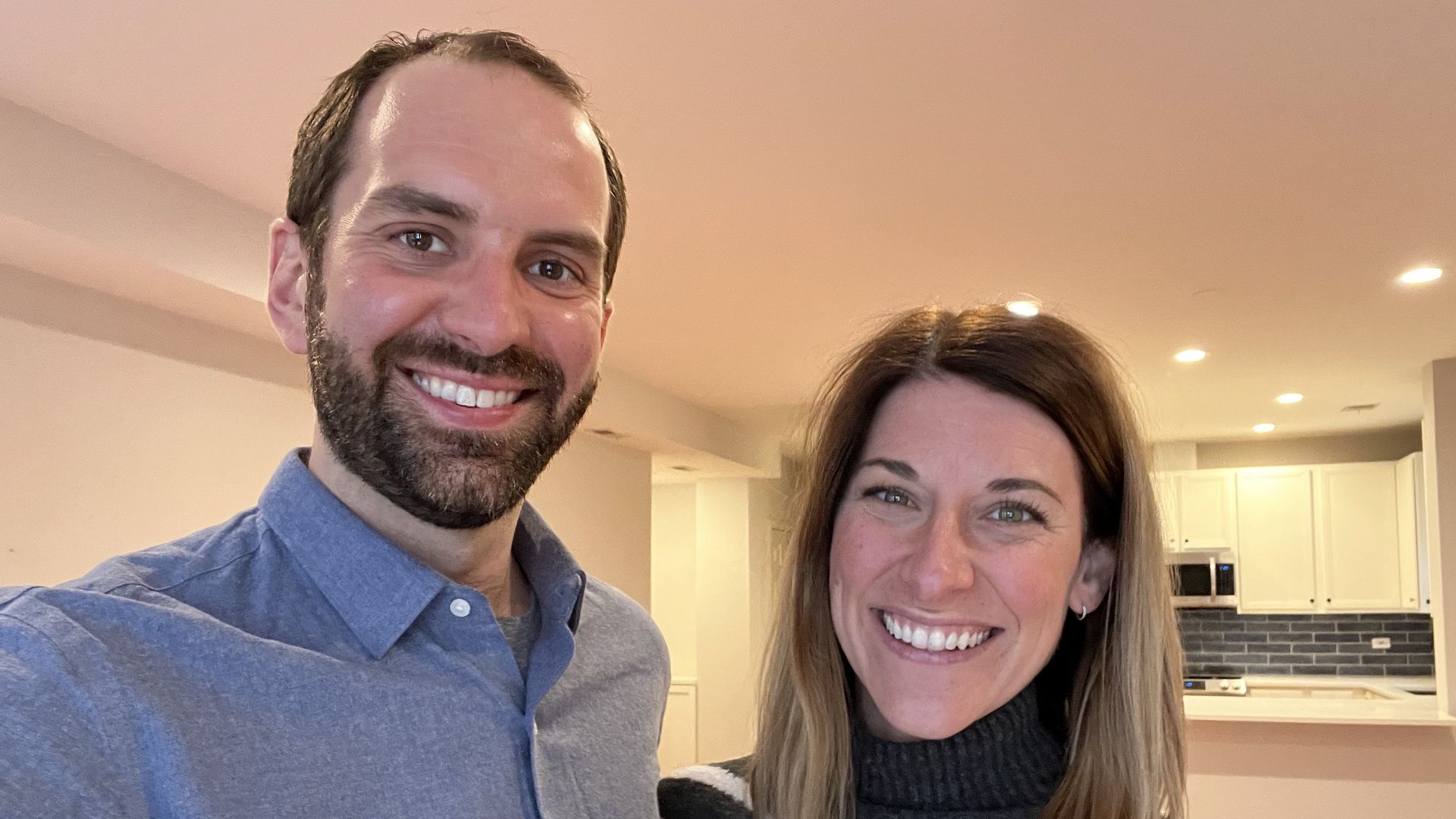 Man and woman smiling with kitchen in background.