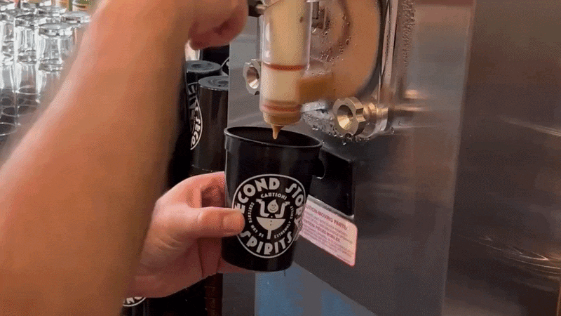 A frozen brown cocktail pours into a black plastic cup that reads Second Story Spirits. 