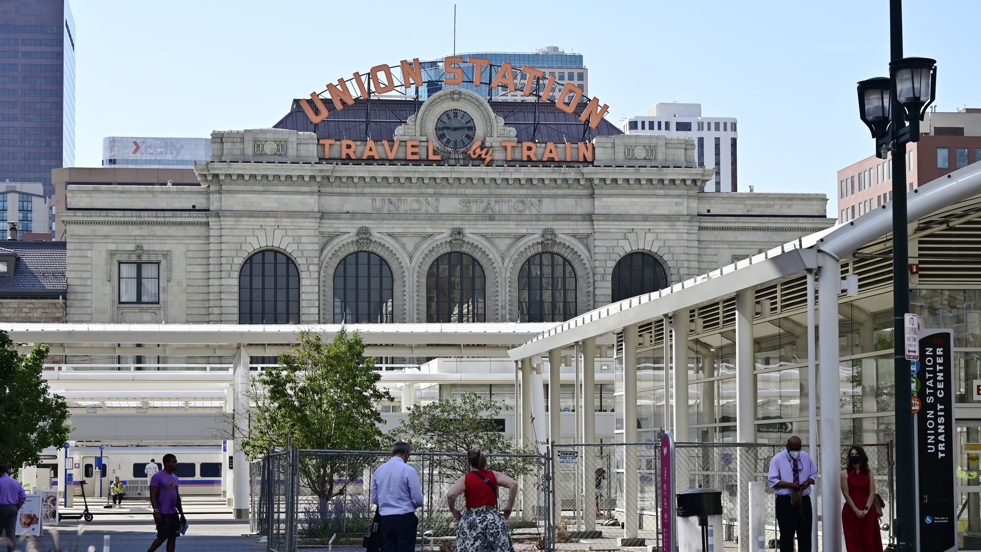 A massive, gray brick building with the words UNION STATION and TRAVEL BY TRAIN written in large, orange letters.