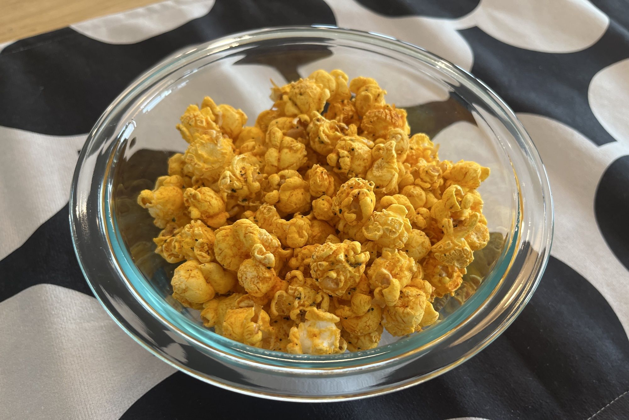 Clear glass bowl filled with bright orange cheese-flavored popcorn on a black and white patterned surface.