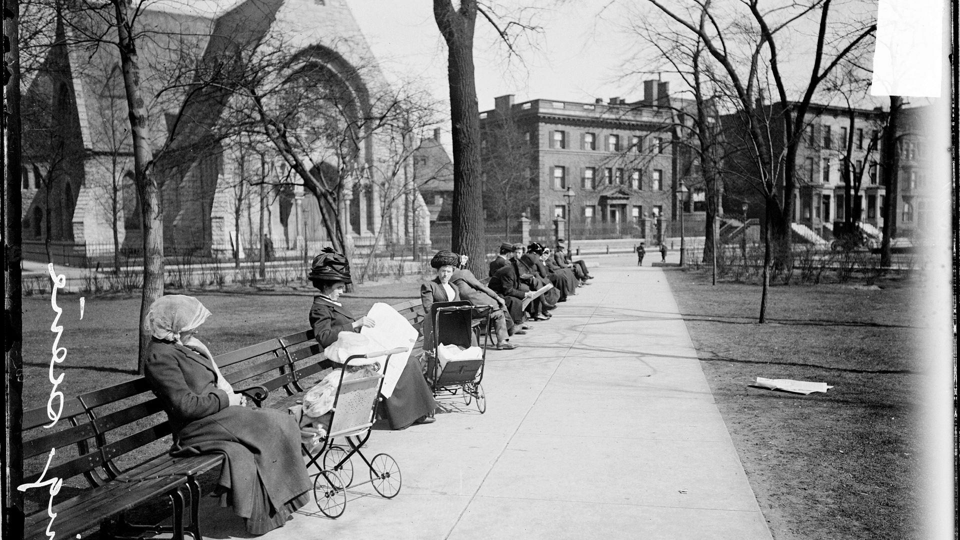 Photo of a women with buggies sitting on park benches in park. 
