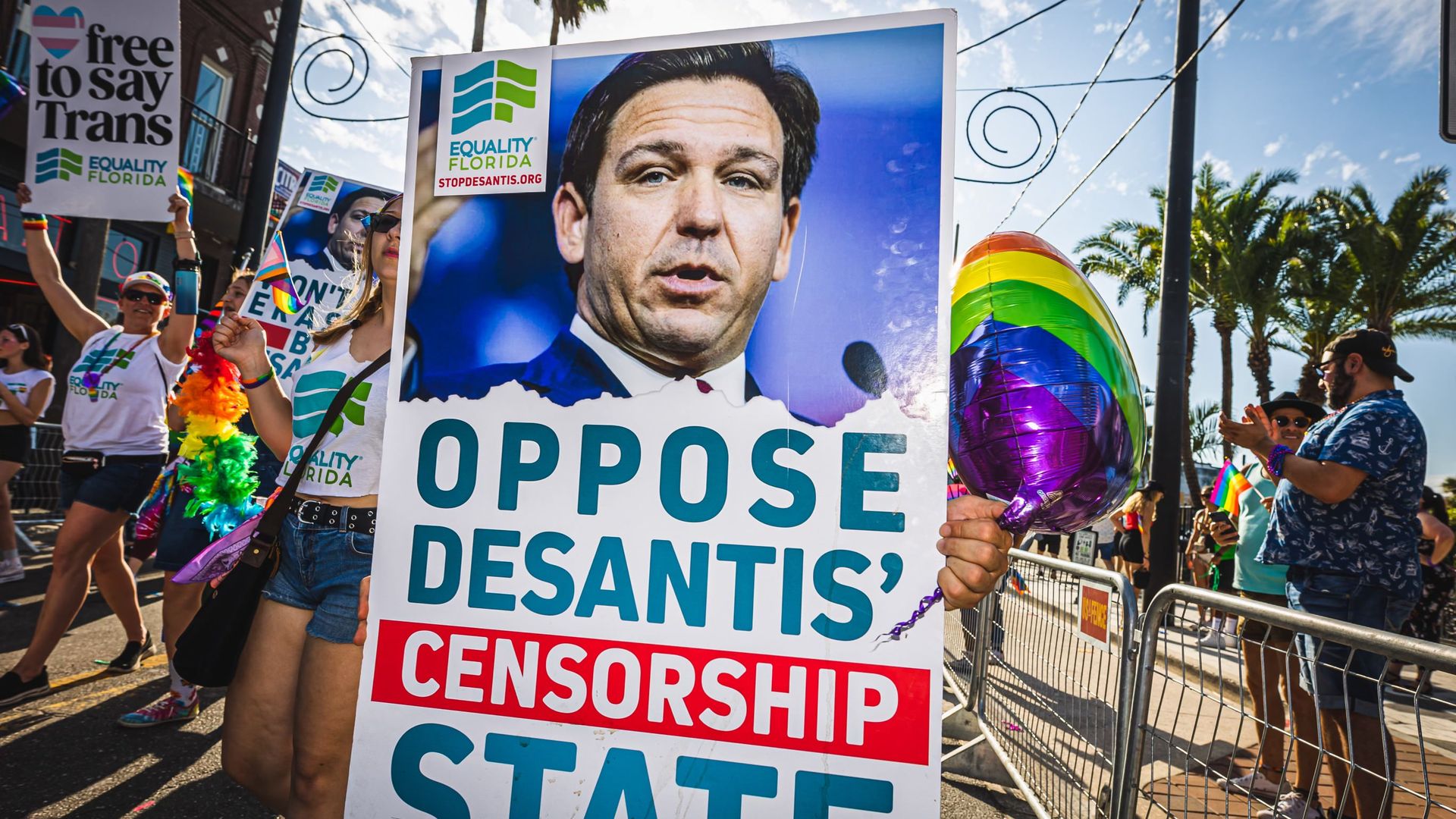 Someone marching in the Pride parade with a sign reading "oppose desantis' censorship state" with a picture of the governor and the Equality Florida logo