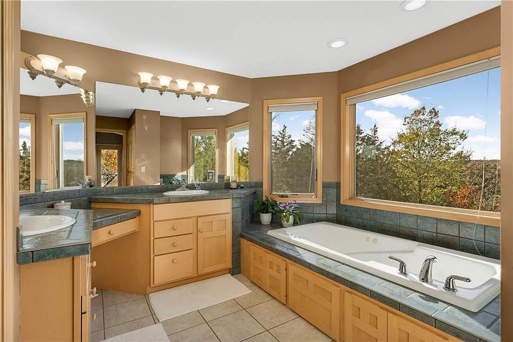 A master bathroom with a tub, counter, beige walls and large windows showing a river.