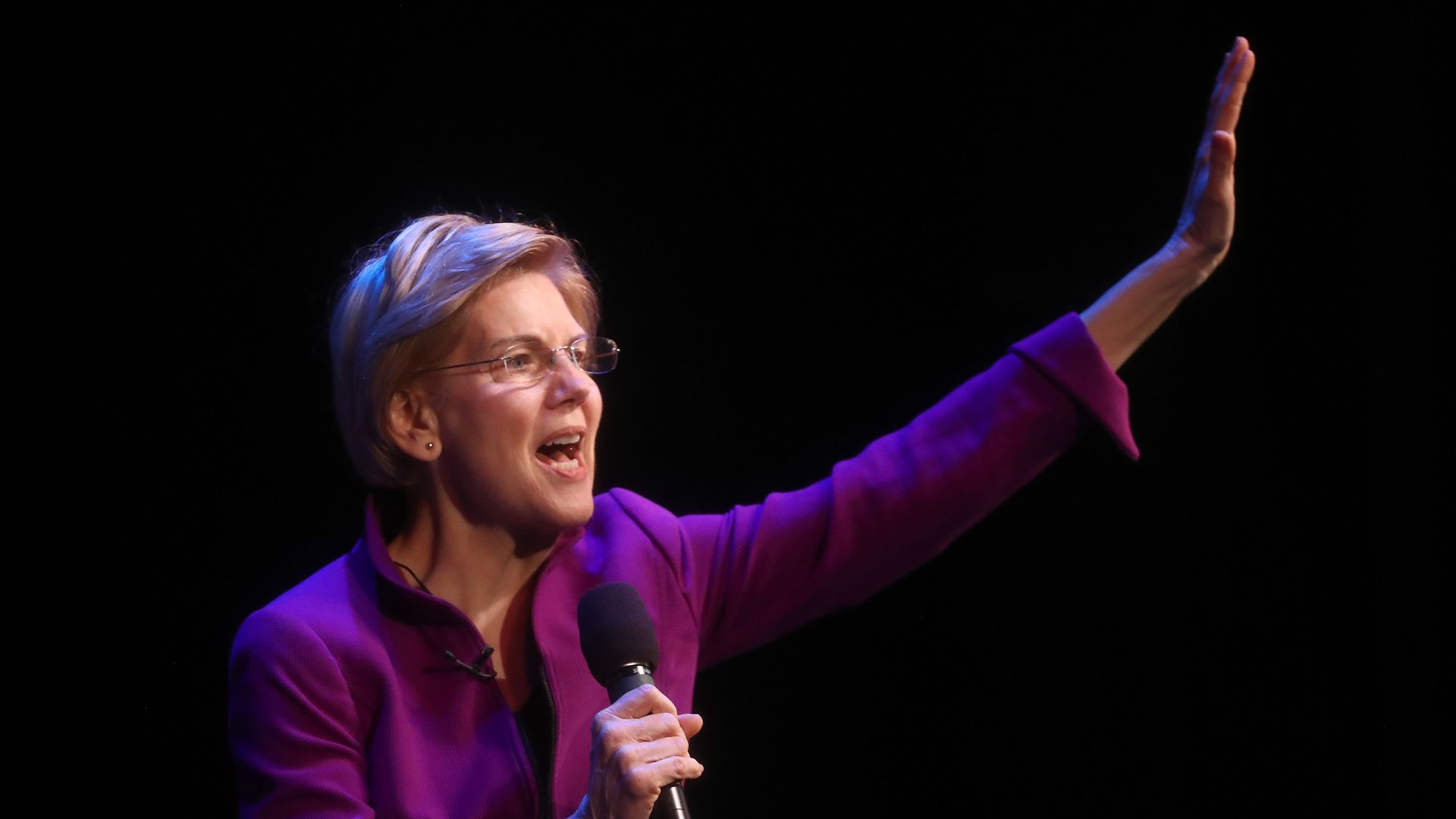 Elizabeth Warren give a speech with her arm raised up