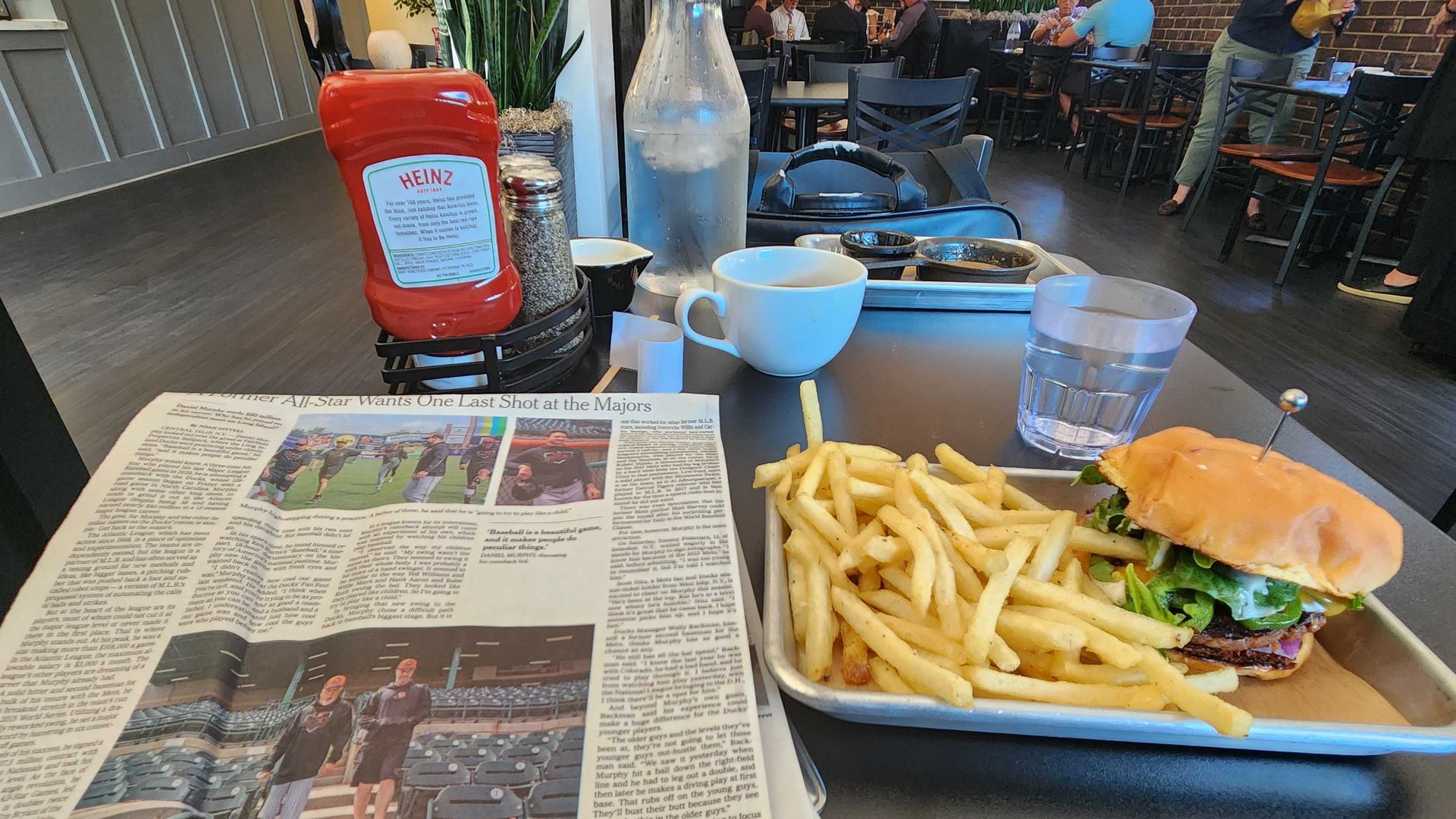A vegan hamburger and fries, a newspaper, and other table settings at a diner. 