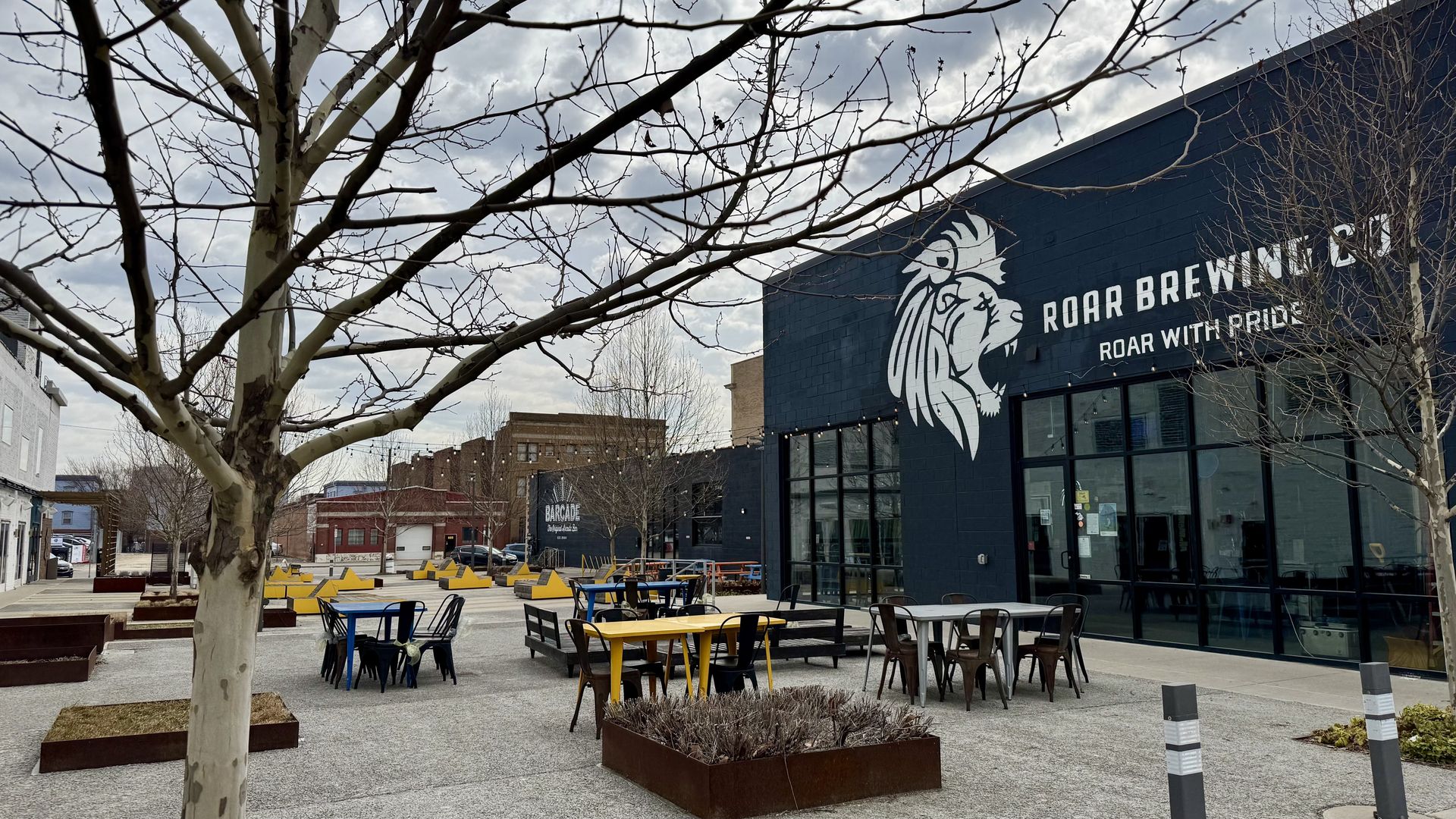 Patio chairs alongside trees and planters next to the brewery's building