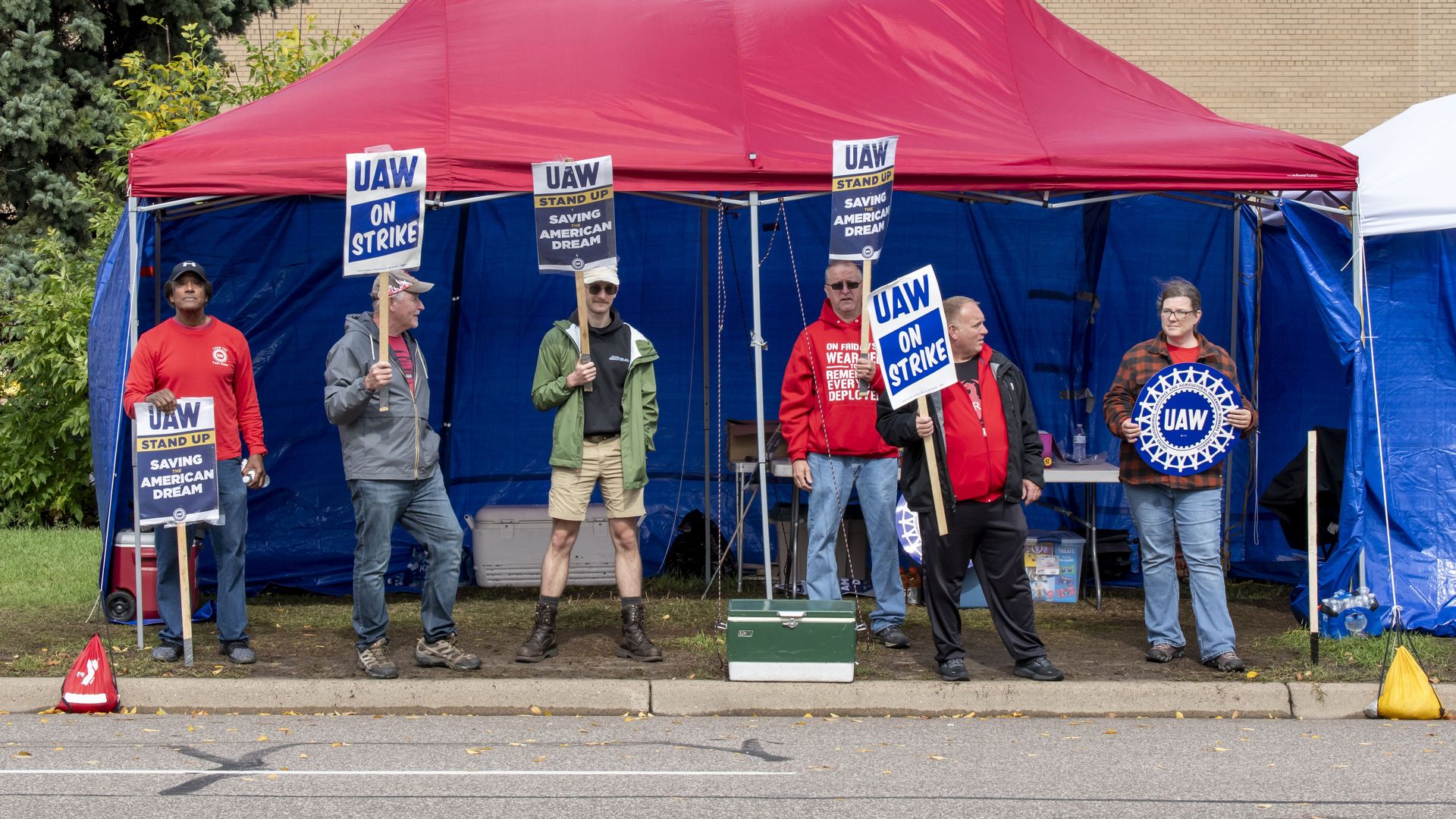 UAW picketers hold signs as they stand under a red tent