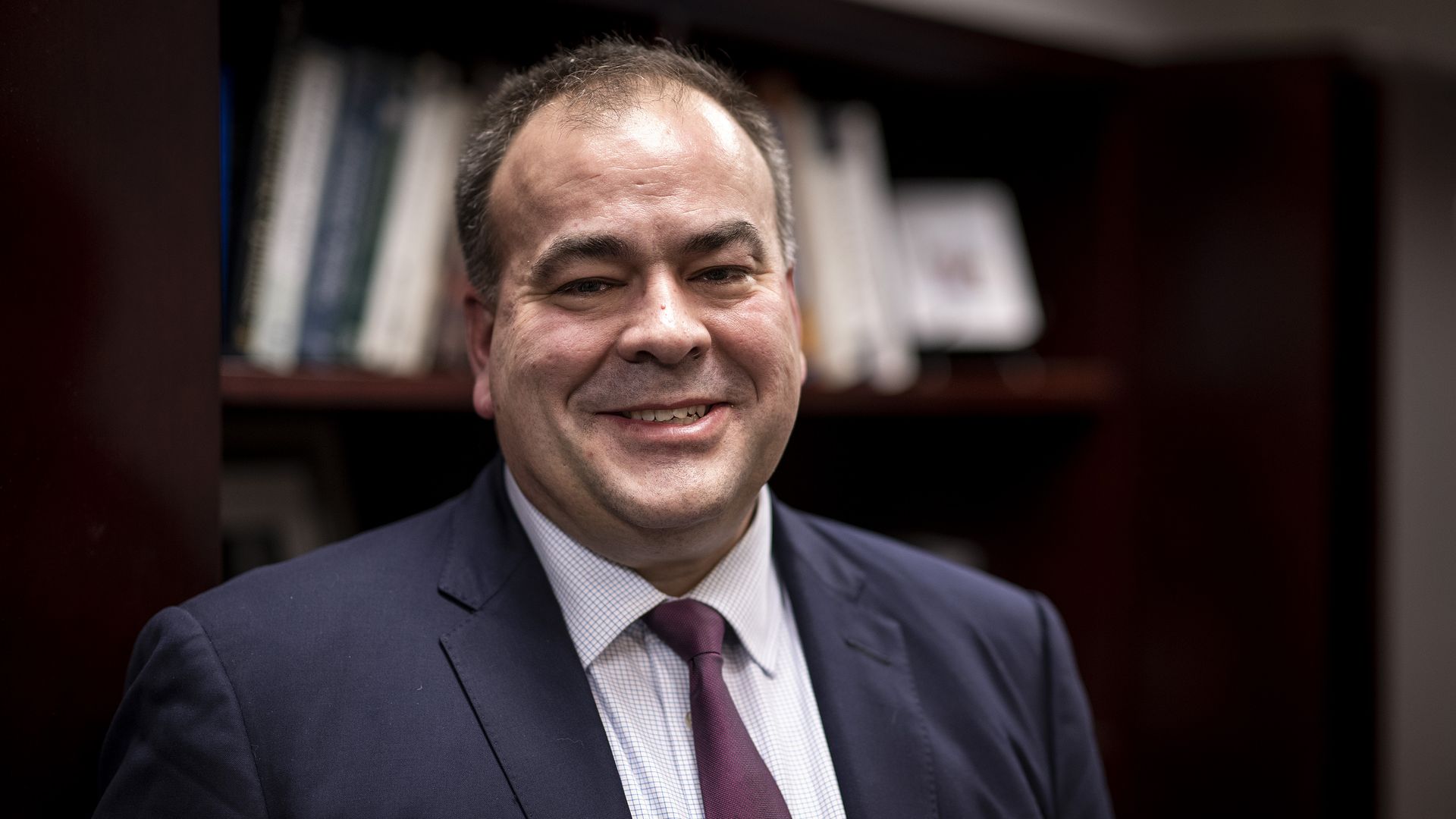 Photo of a man smiling while wearing a suit and tie.
