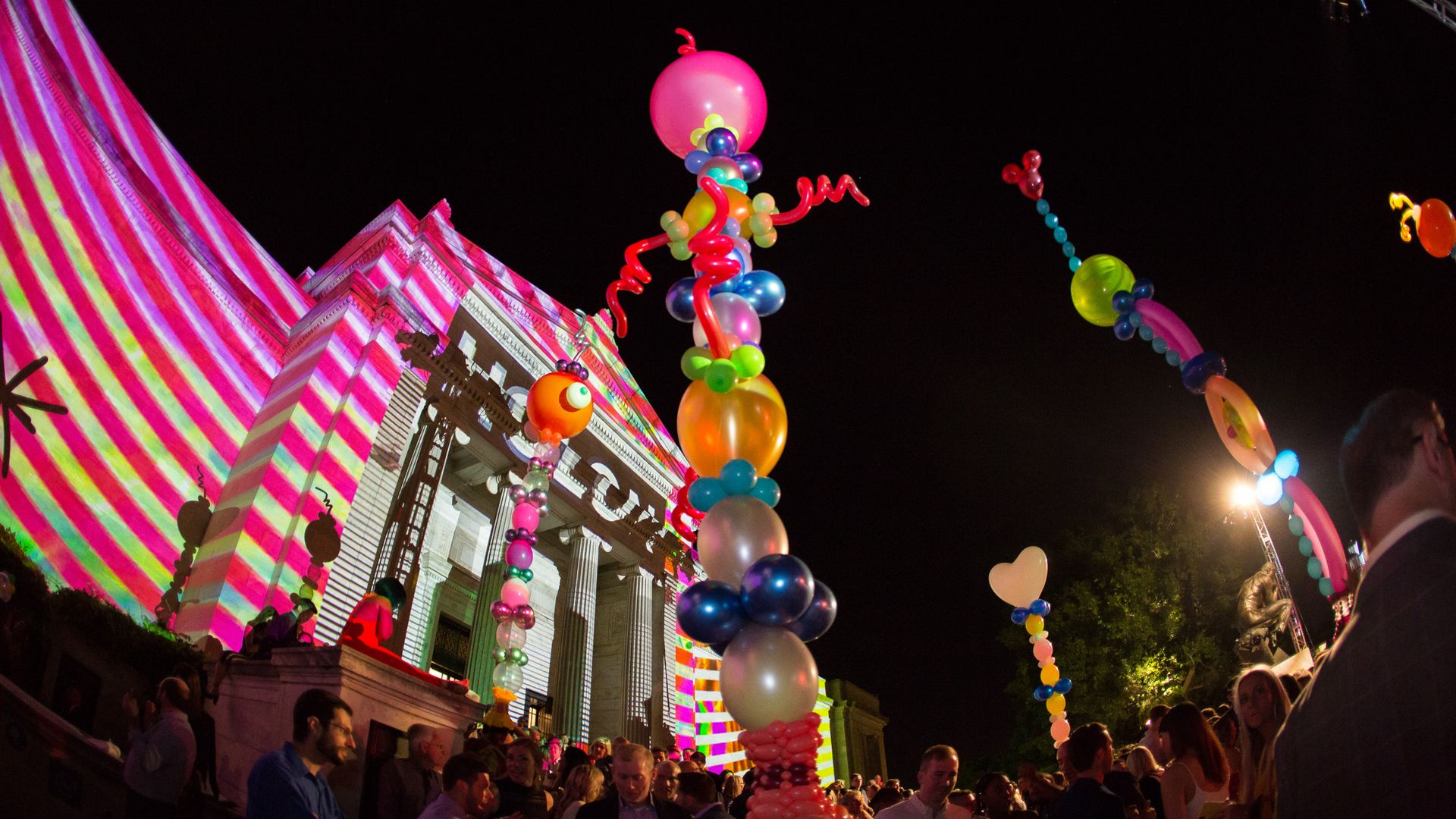 Museum covered in projected art behind a huge series of ballon shapes.