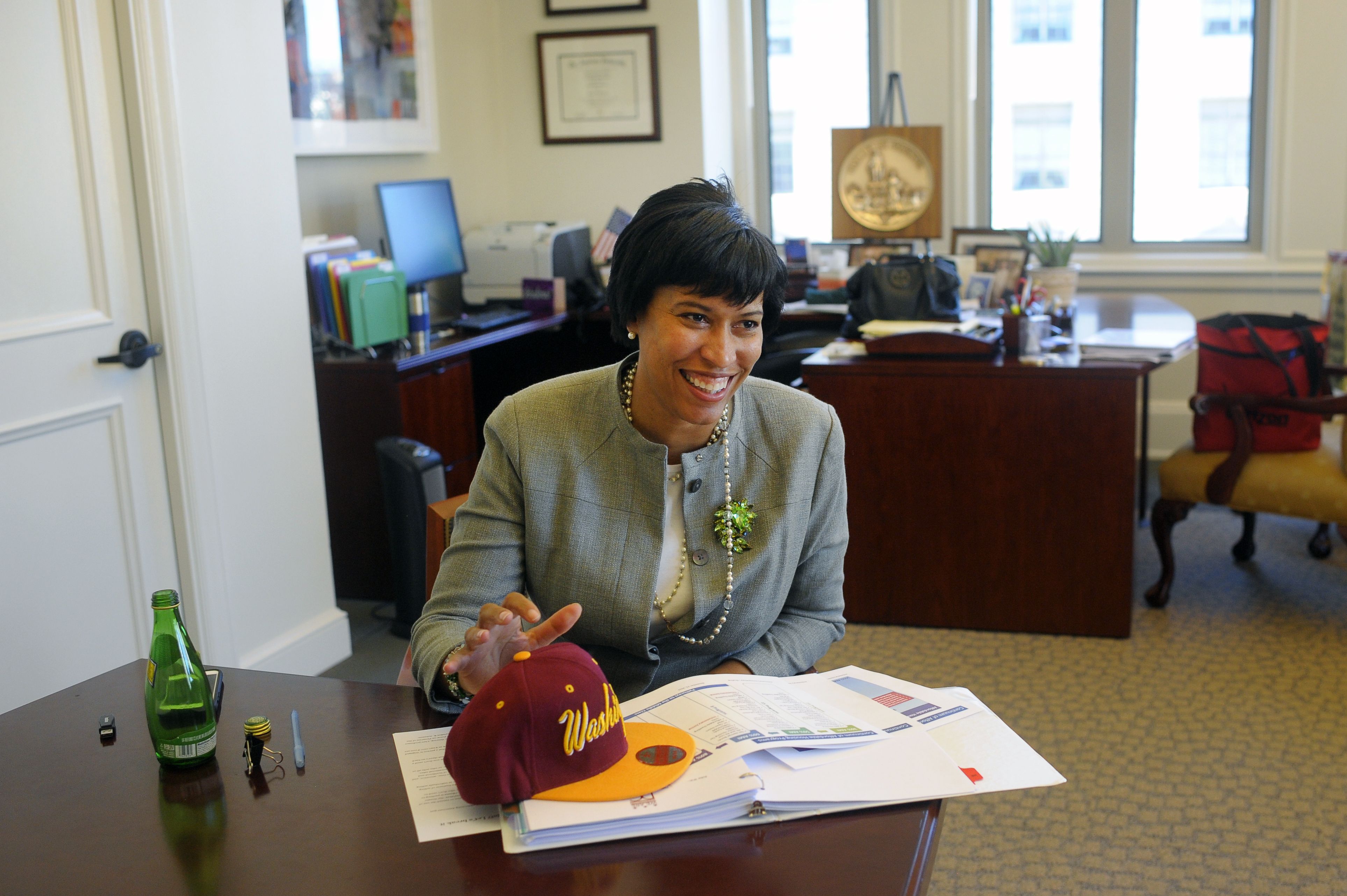 Muriel Bowser sits at a desk with a burgundy and gold cap with Washington imprinted on it, on top of her papers.