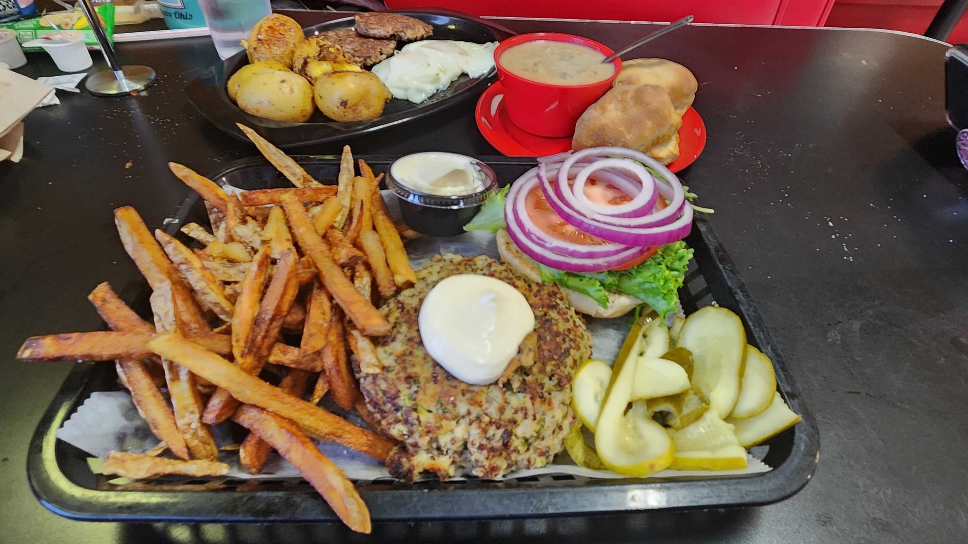 A hamburger, fries, and breakfast platter on a diner table. 