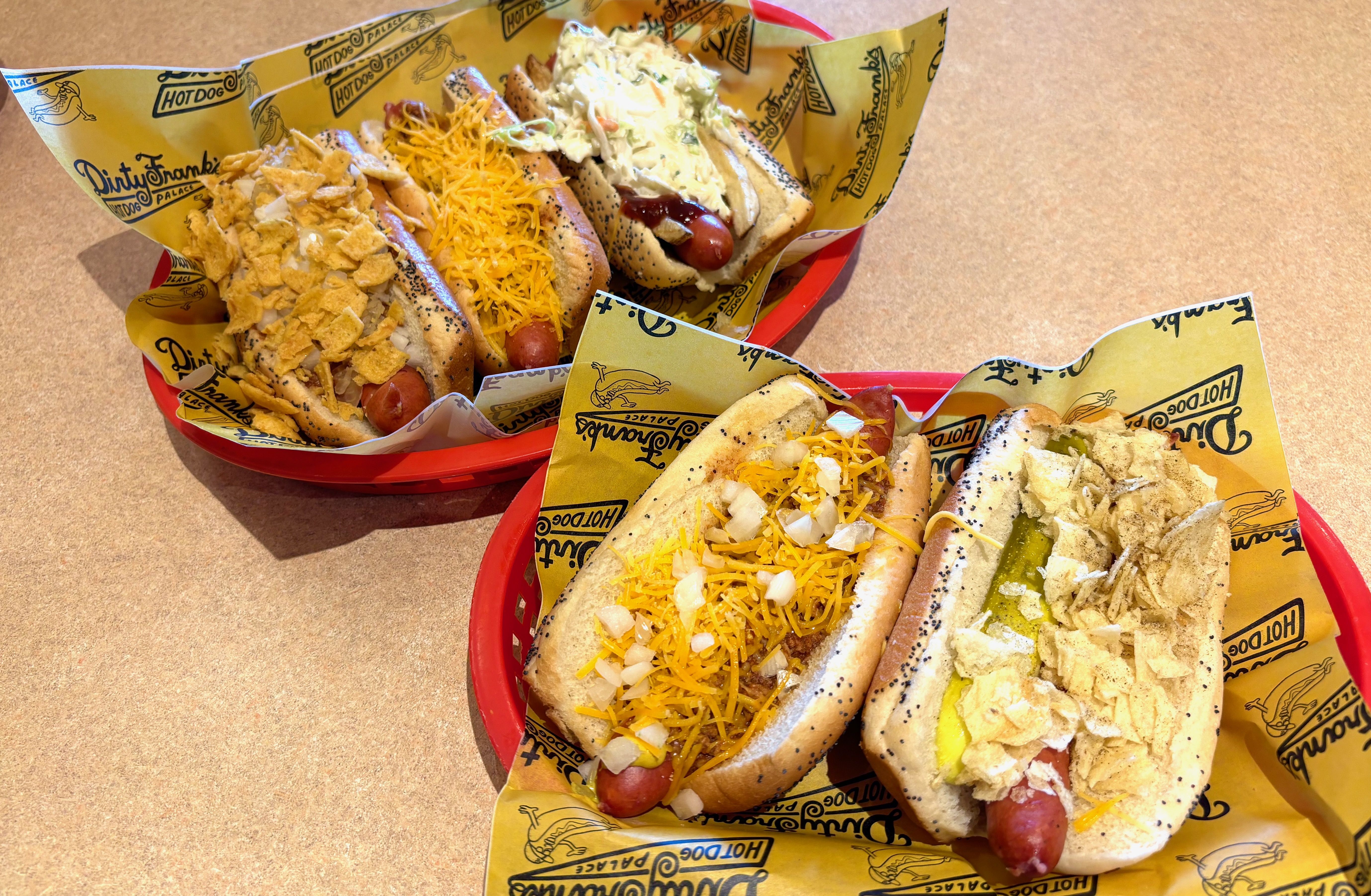 Five hot dogs in baskets covered in toppings like cheese, potato chips and coleslaw
