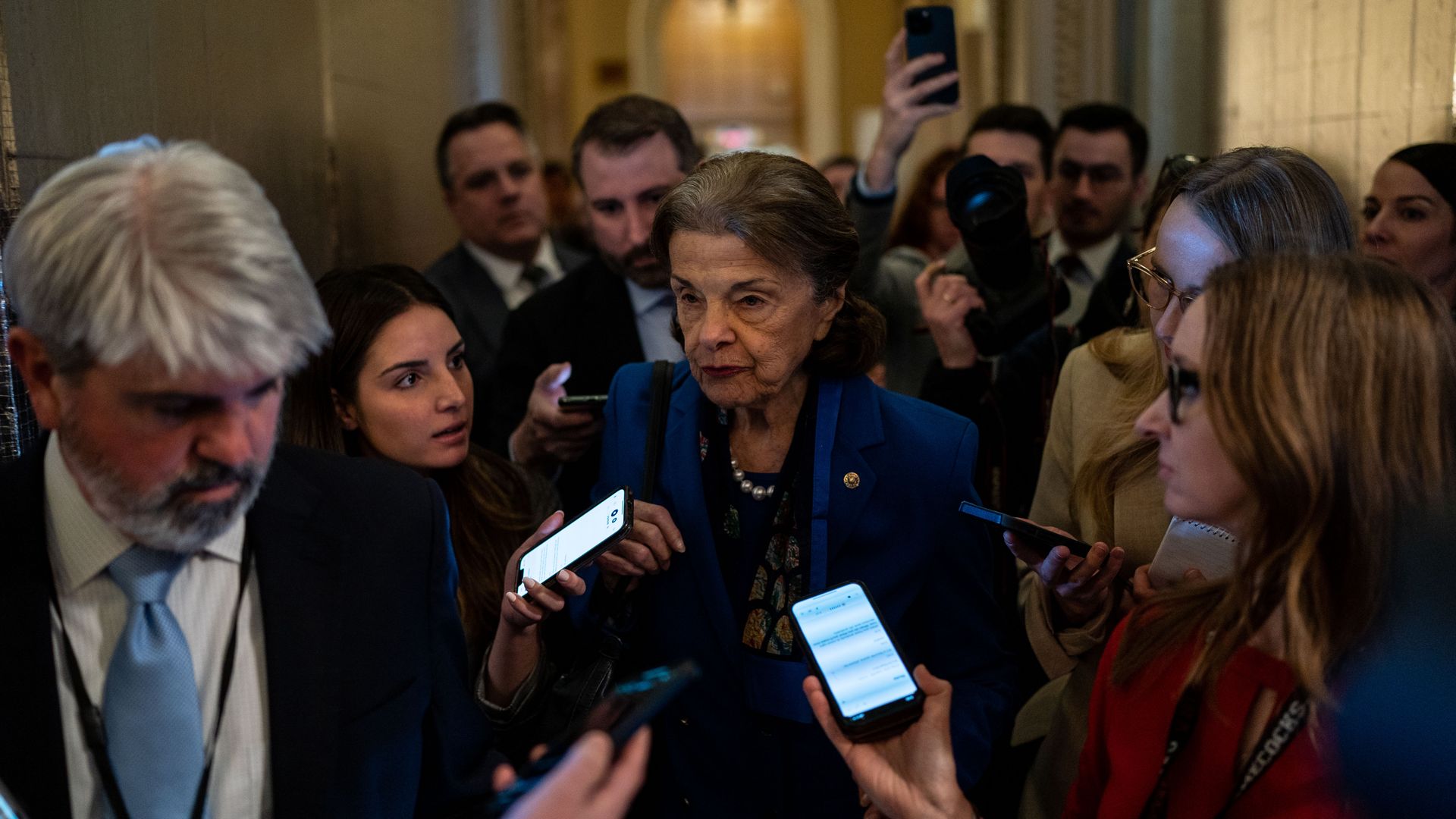Sen. Dianne Feinstein, wearing a blue suit jacket, black shirt and pearl necklace, speaks to a throng of reporters outside the Senate chamber.