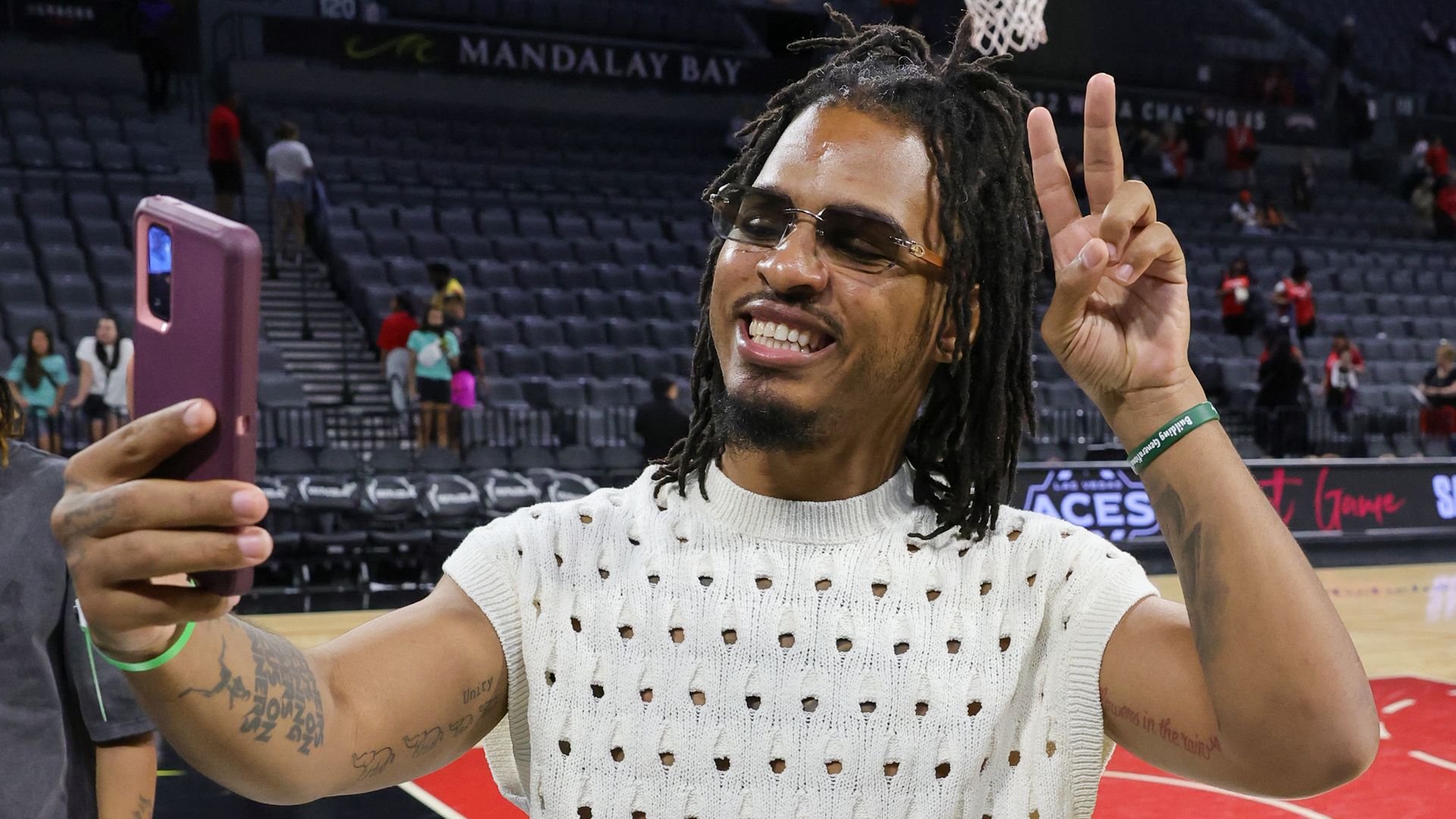 a man holding a purple-cased iPhone smiling with the peace sign up.