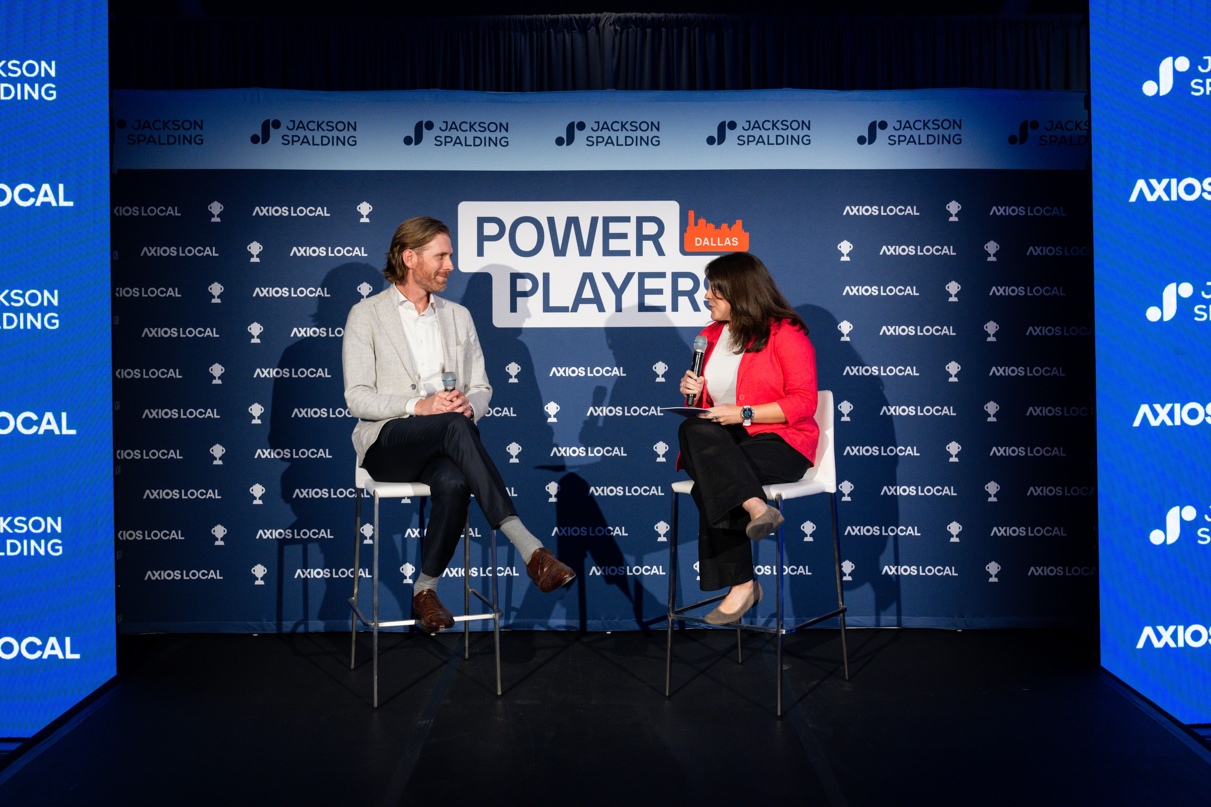 two people sit on a stage and talk to the crowd