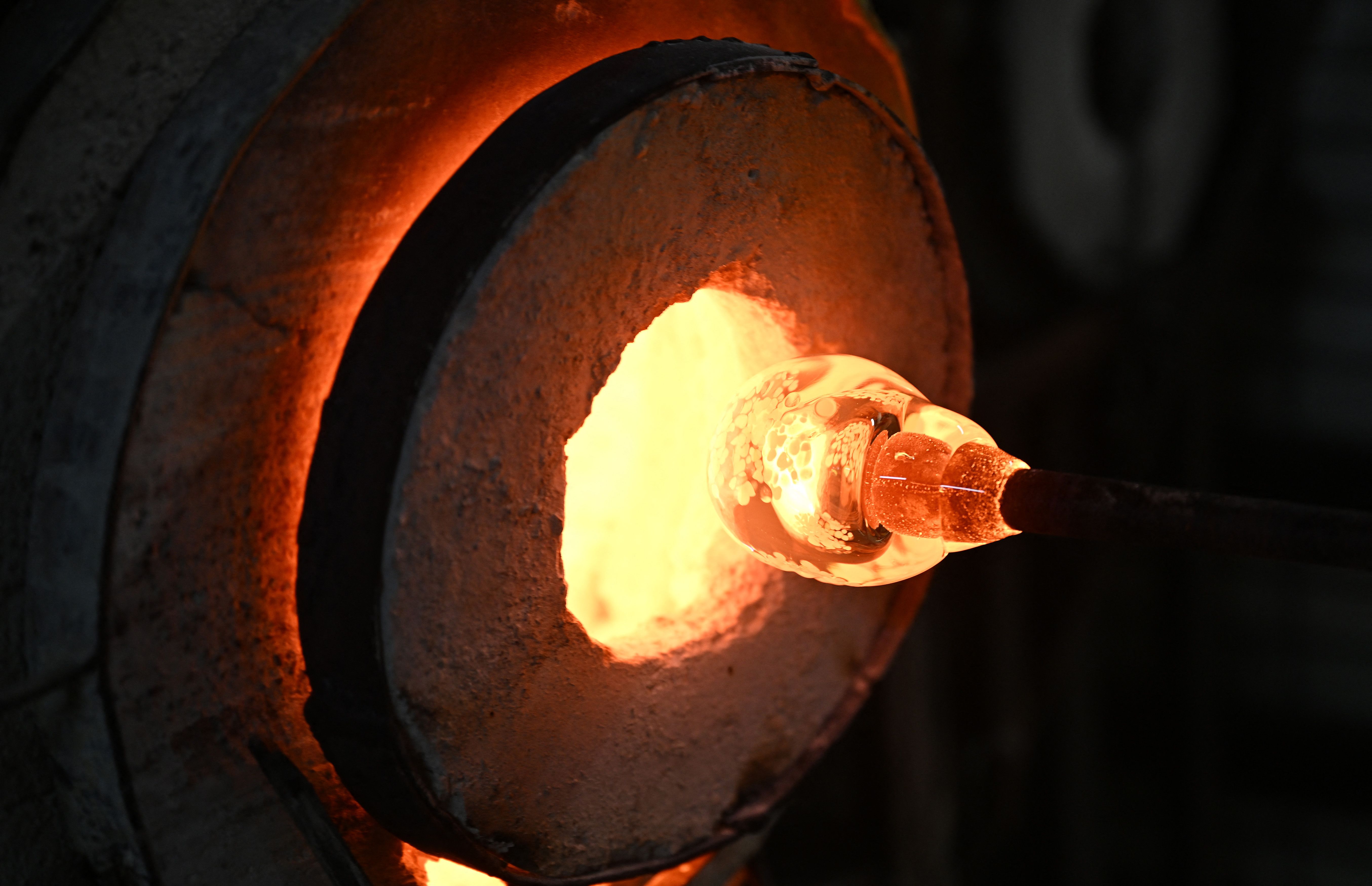 Molten yellow-orange glass on the end of a rod is placed inside a white-hot circular furnace