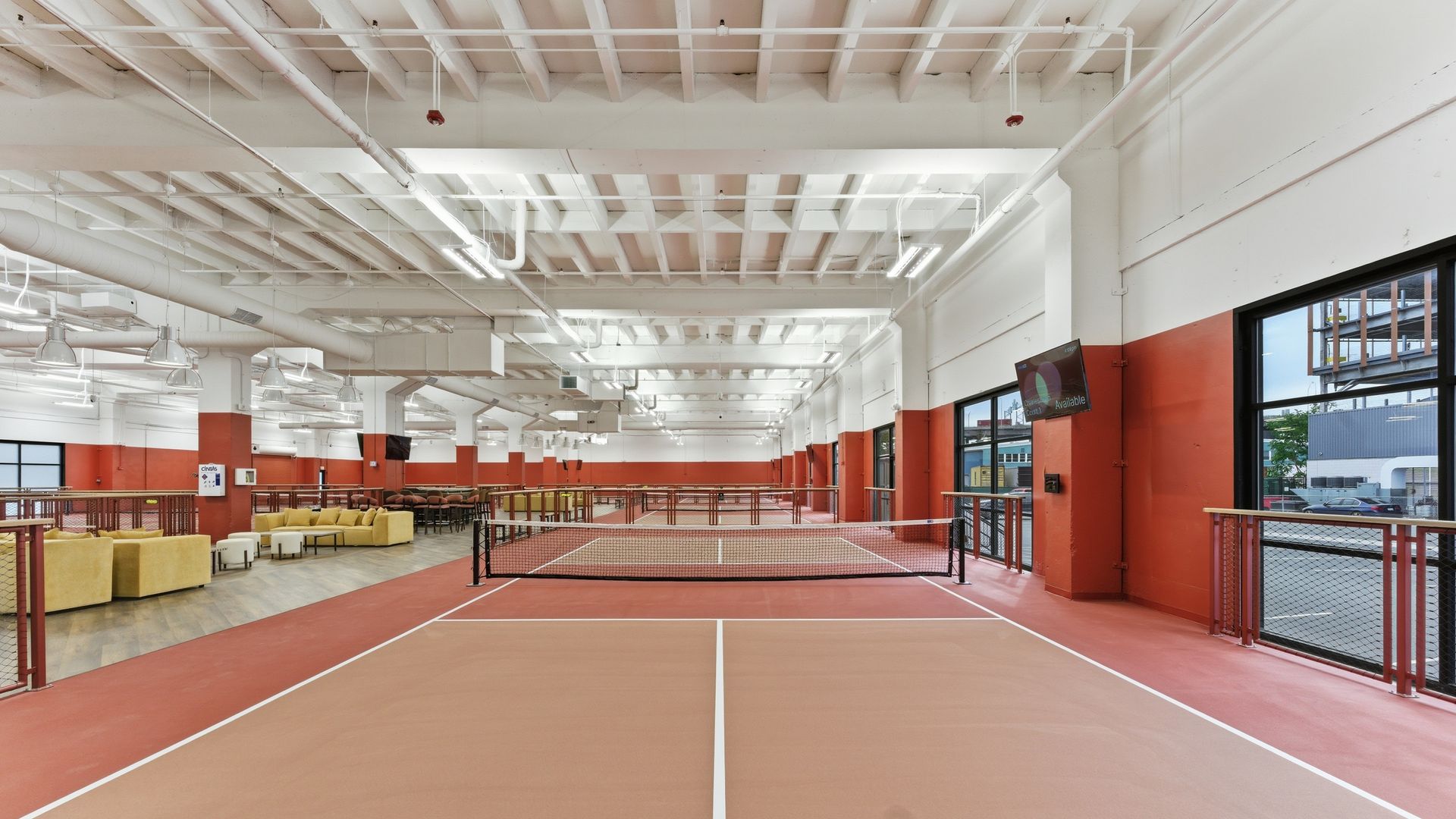 Wide view of an empty indoor gym with several pickleball courts and nets. 