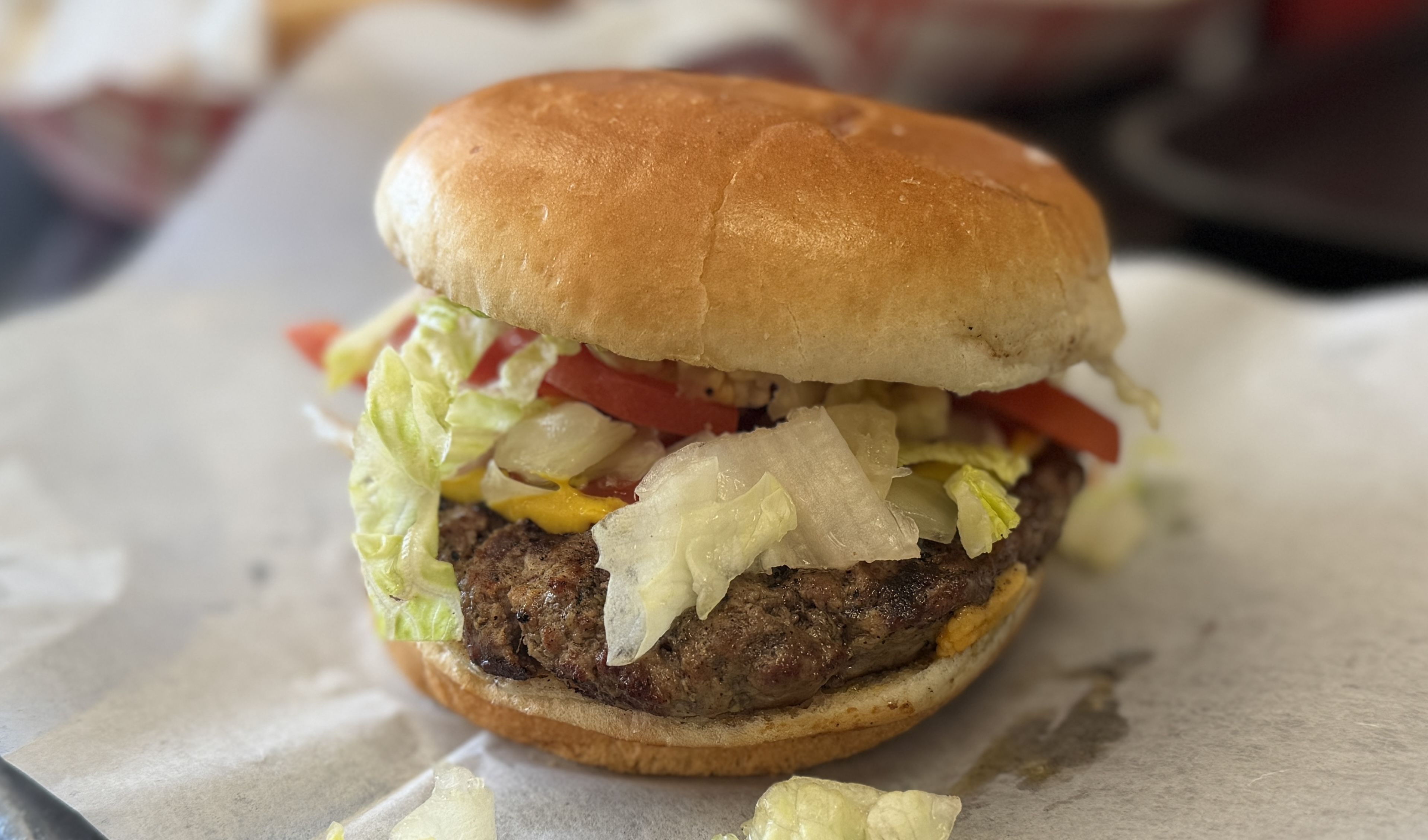 A hamburger on a toasted bun with a beef patty, shredded lettuce, tomato slices, and melted cheese, resting on parchment.