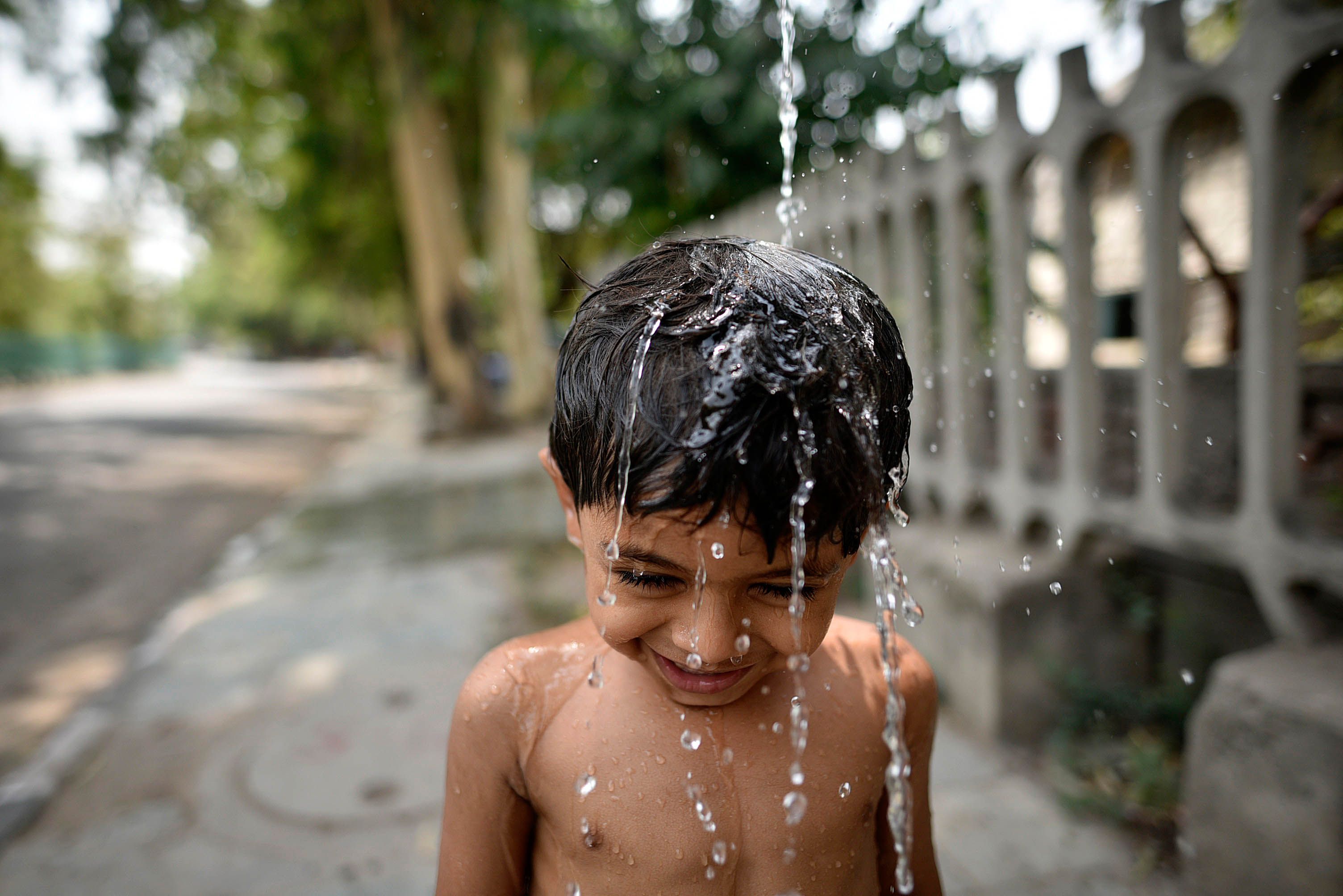 A boy cools himself off while he enjoys taking a bath on a hot afternoon, near Nizamuddin, on June 2, 2019 in New Delhi, India. 