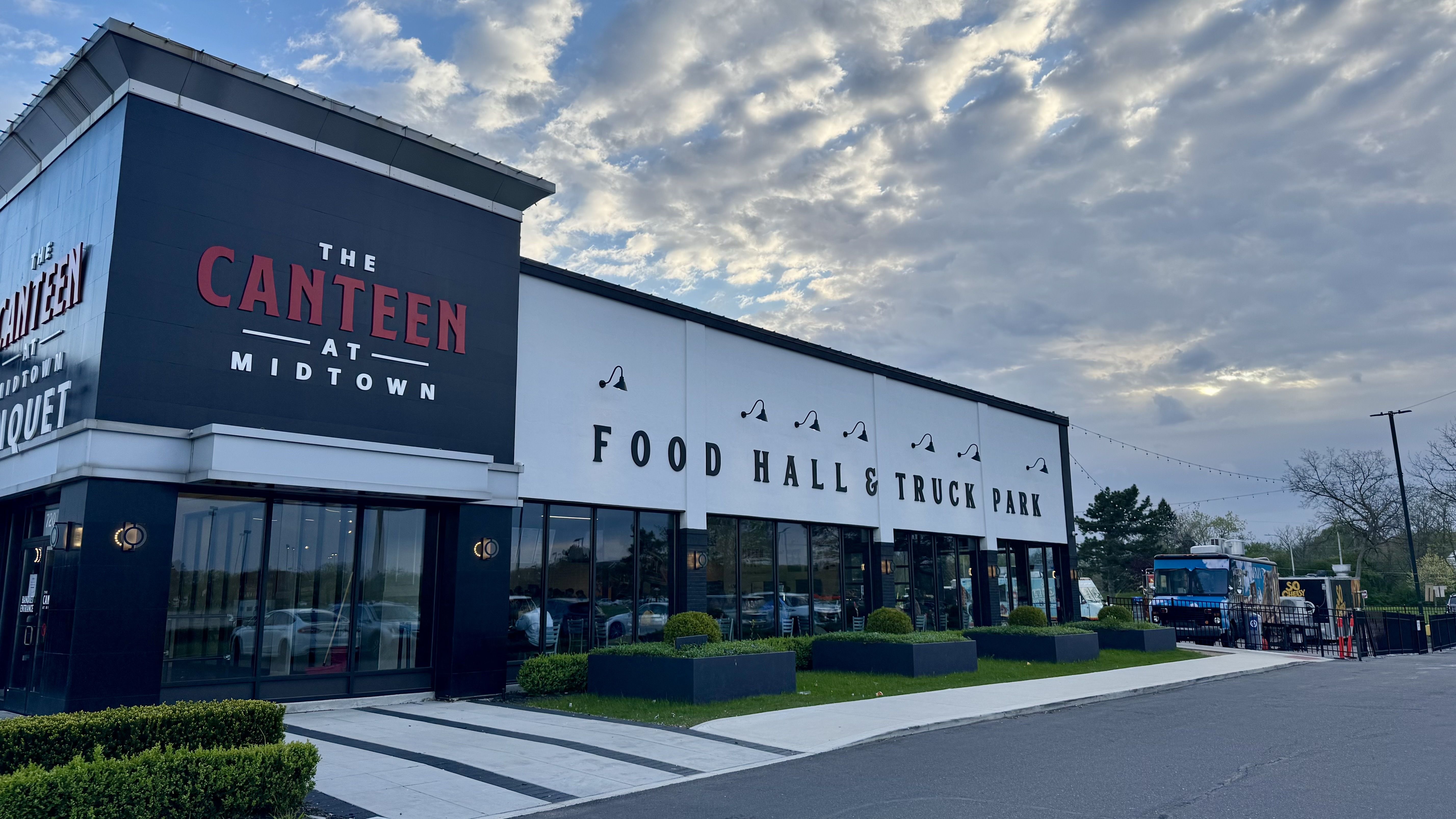 Modern storefront with a dark blue wall displaying "THE CANTEEN AT MIDTOWN" in red and a white wall sign reading "FOOD HALL & TRUCK PARK."