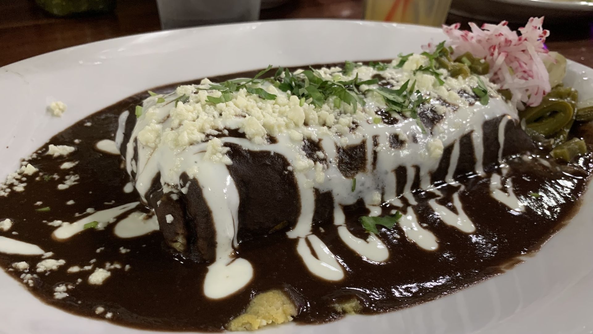 Tamale covered in black mole, sour cream and crumbled cheese on top