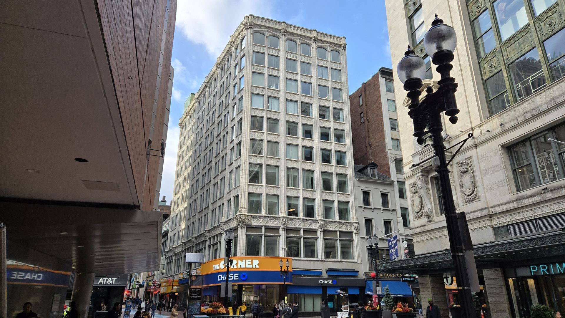 Corner view of a white historic multi-story building with large windows, blue Chase bank signs, an orange "THE CORNER" sign, black street lamps, and pedestrians on a city street.