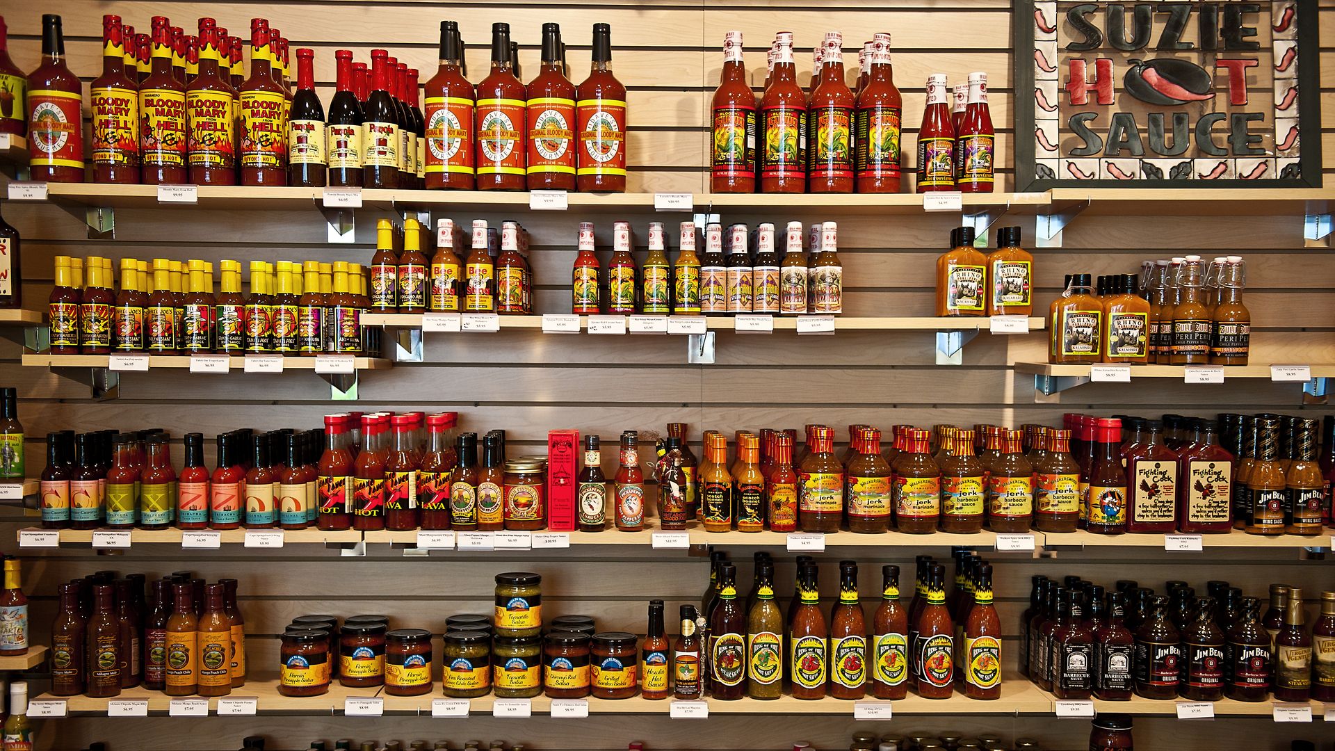 Store shelves stocked floor to ceiling with red hot sauce bottles with red liquid inside and bright labels.