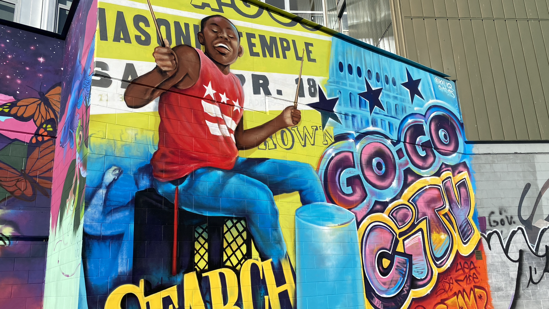 A brightly-colored mural showing a young Black boy playing the drums on an overturned bin.