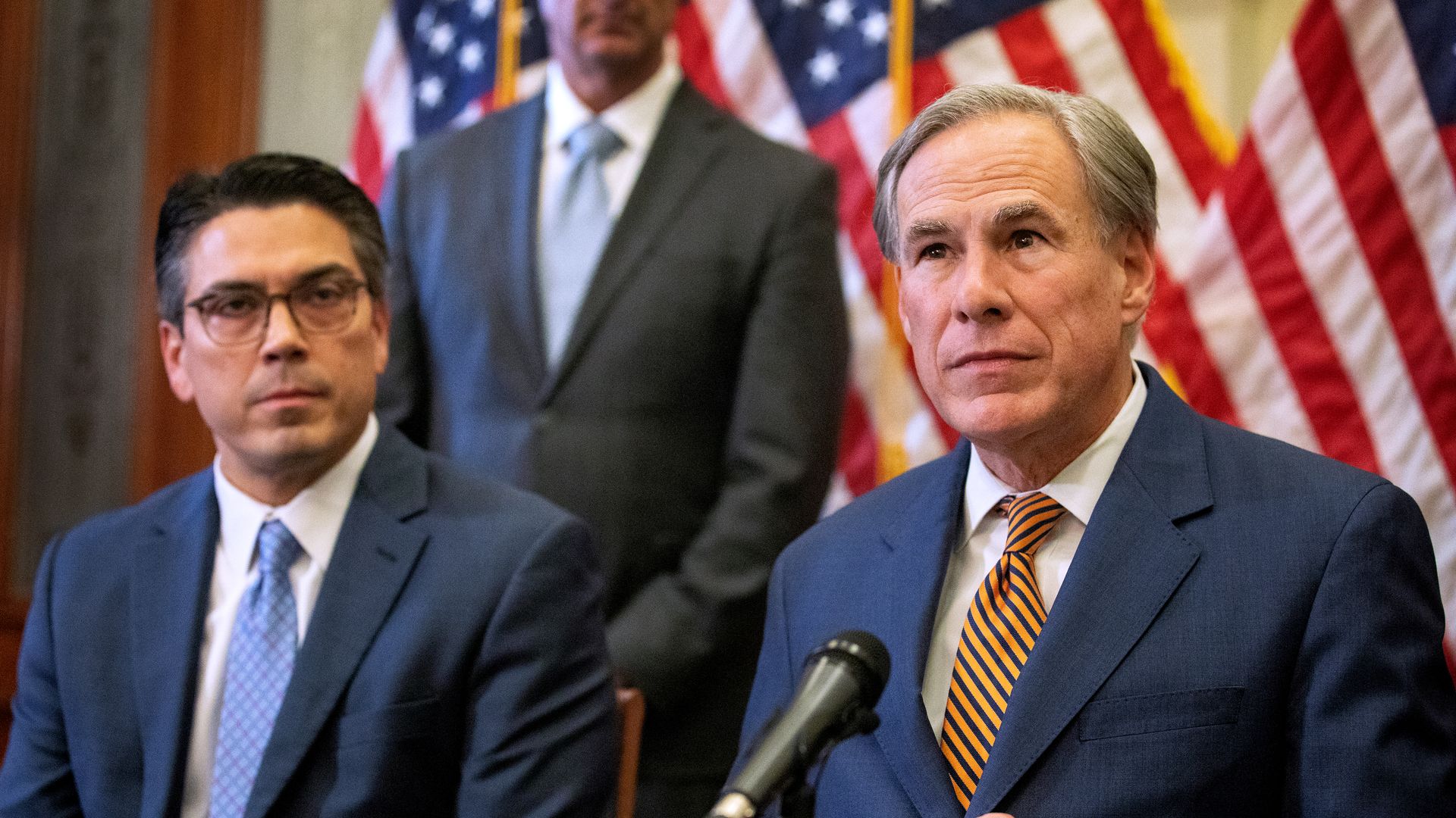 Photo of Greg Abbott and Chris Paddie sitting at a table with the American flag behind them