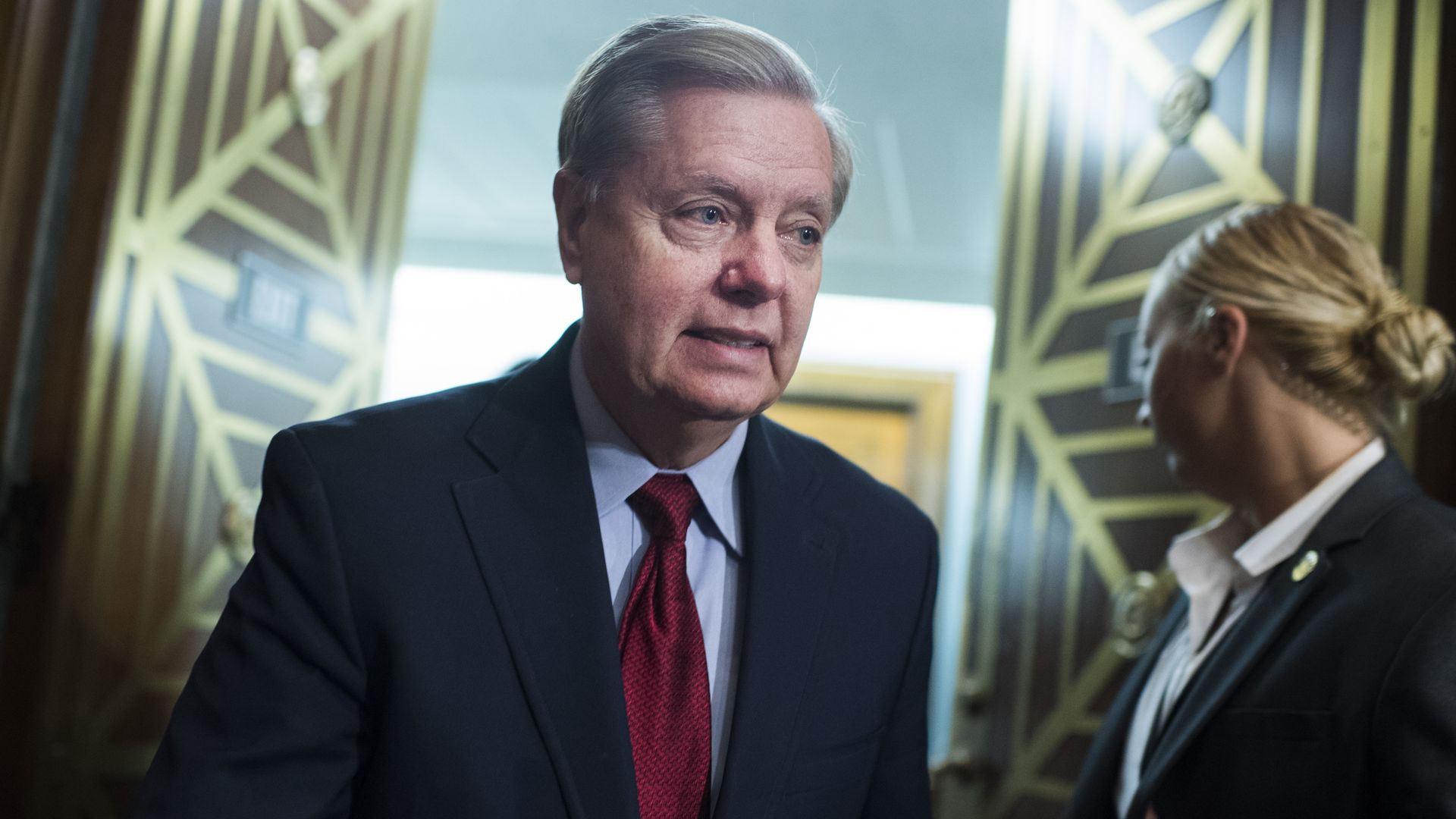 In this image, Graham walks in a suit through an open door