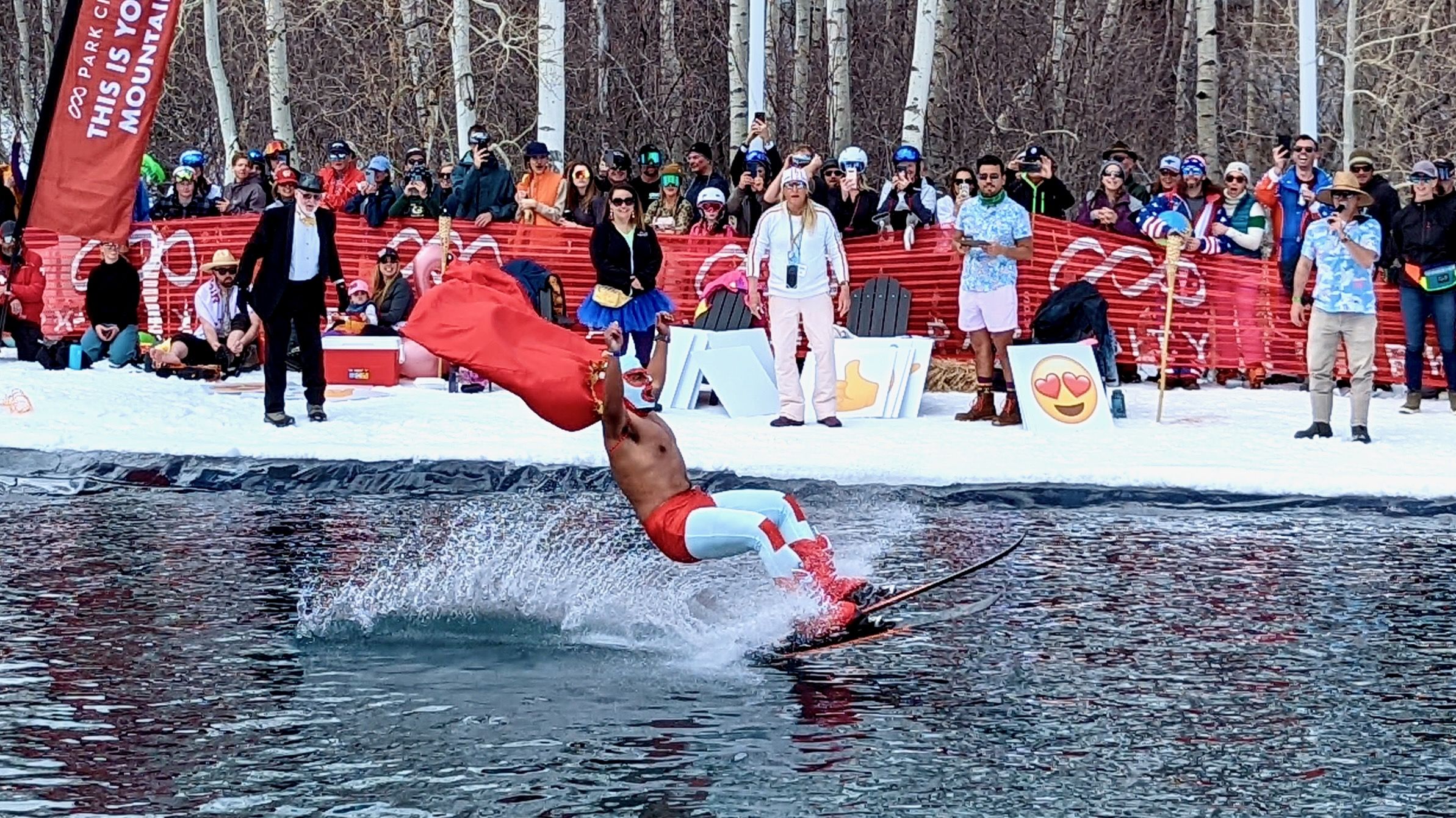 A skier costumed as a Mexican wrestler coasts across a pond of water at the bottom of a ski slope.