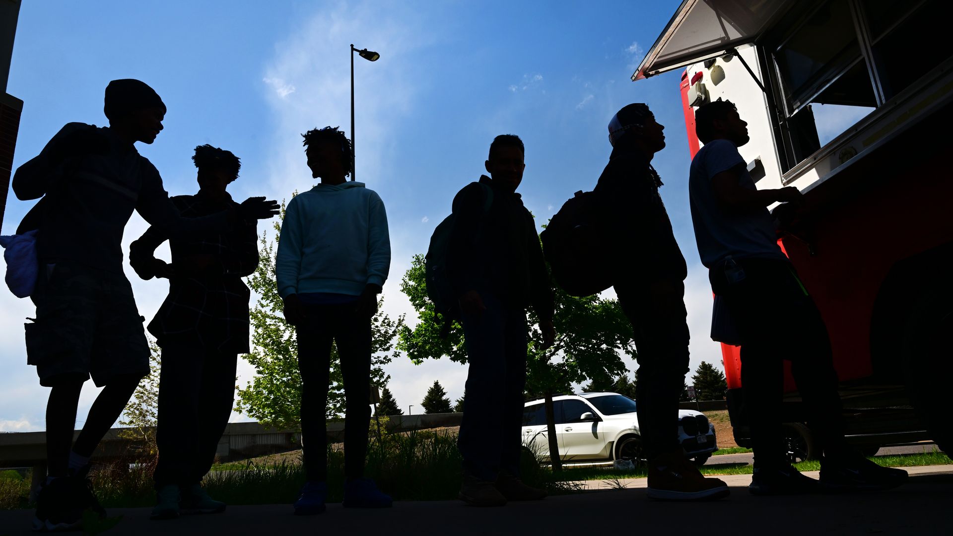 The silhouette of several men waiting in line at a food truck during a sunny day in Denver.  