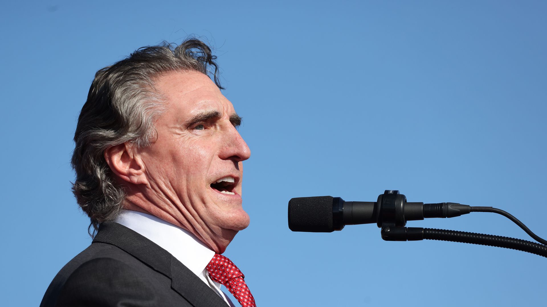Doug Burgum speaks into a microphone with a blue sky behind him.