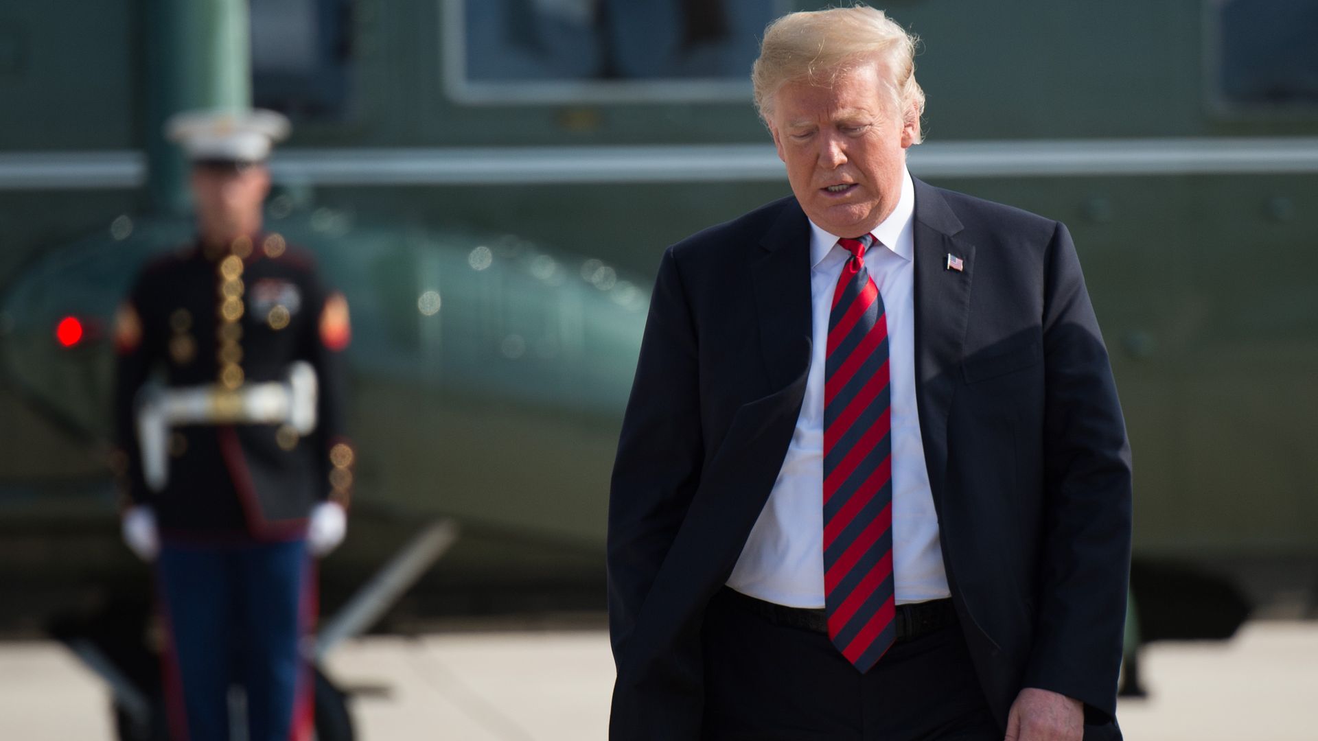 Donald Trump walking away from Air Force One with a dark suit and red and blue striped tie