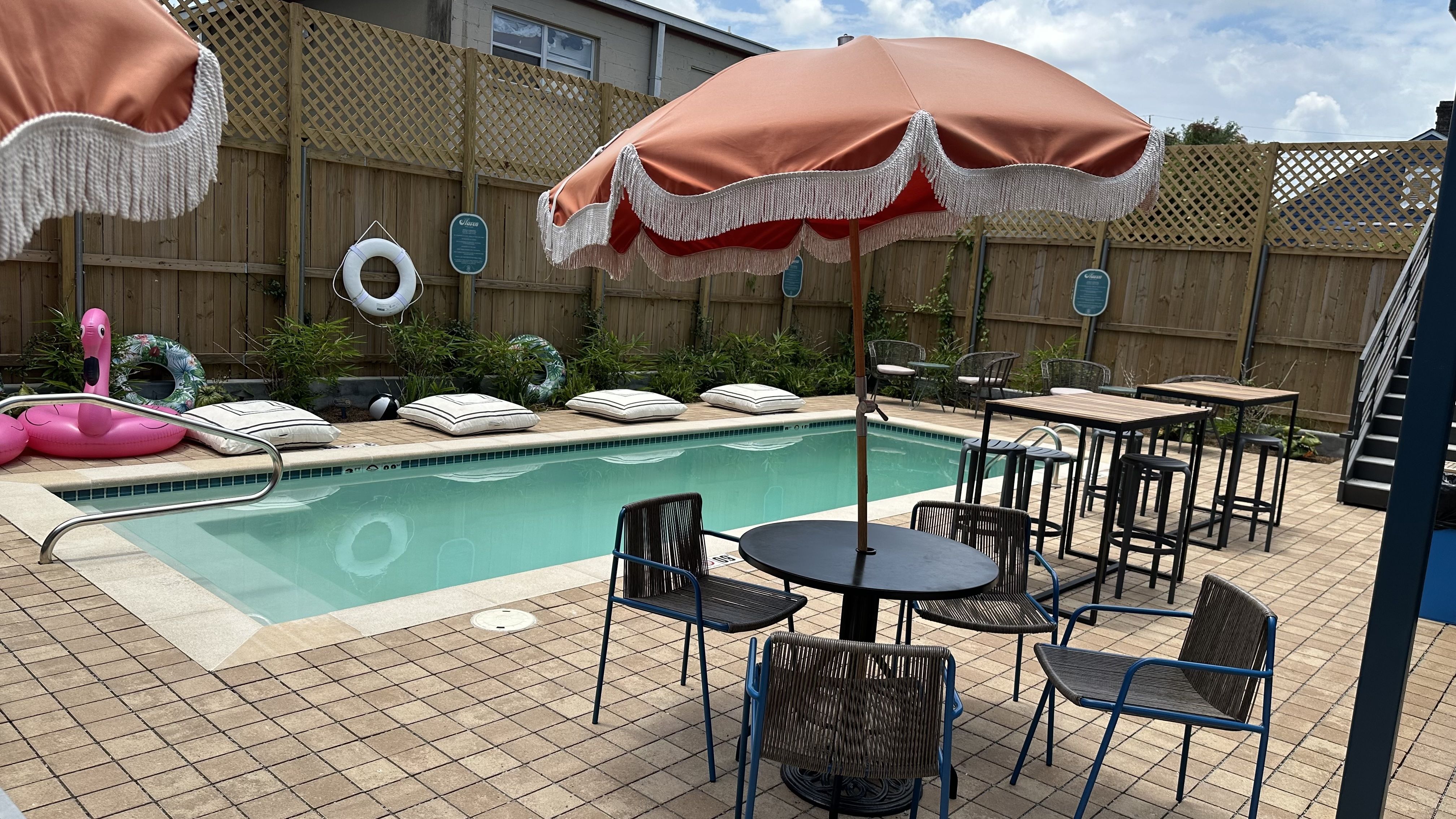 A pool is seen with tables, chairs and umbrellas around it.