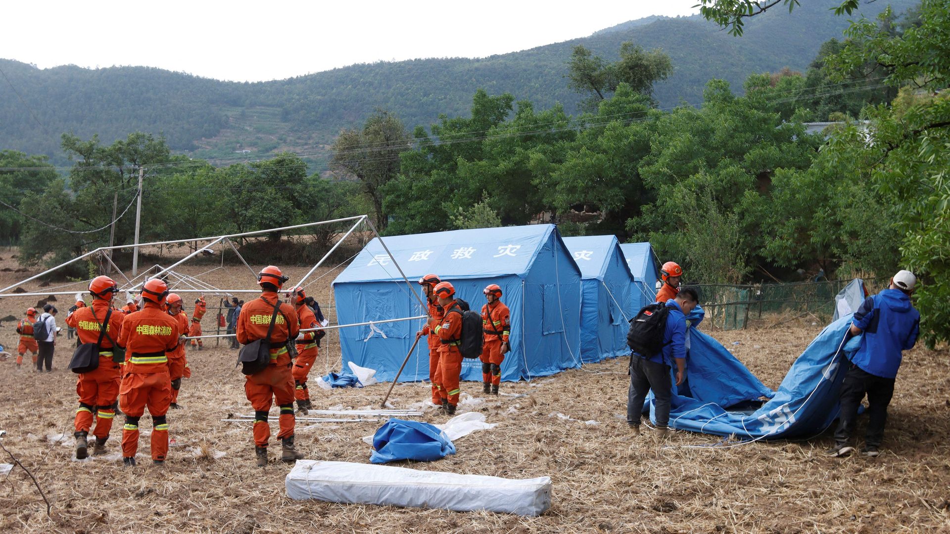 Picture of Chinese rescuers wearing orange uniforms building blue tents 