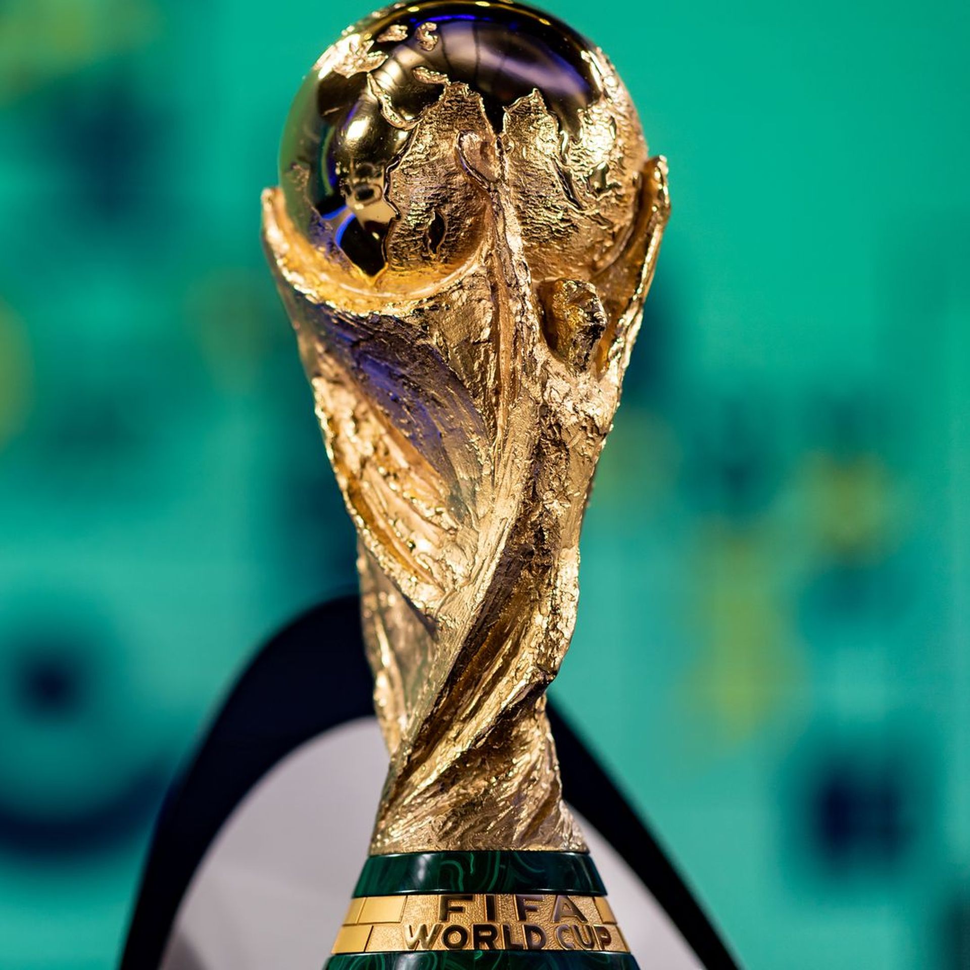 The gold FIFA World Cup trophy with green background behind it. 