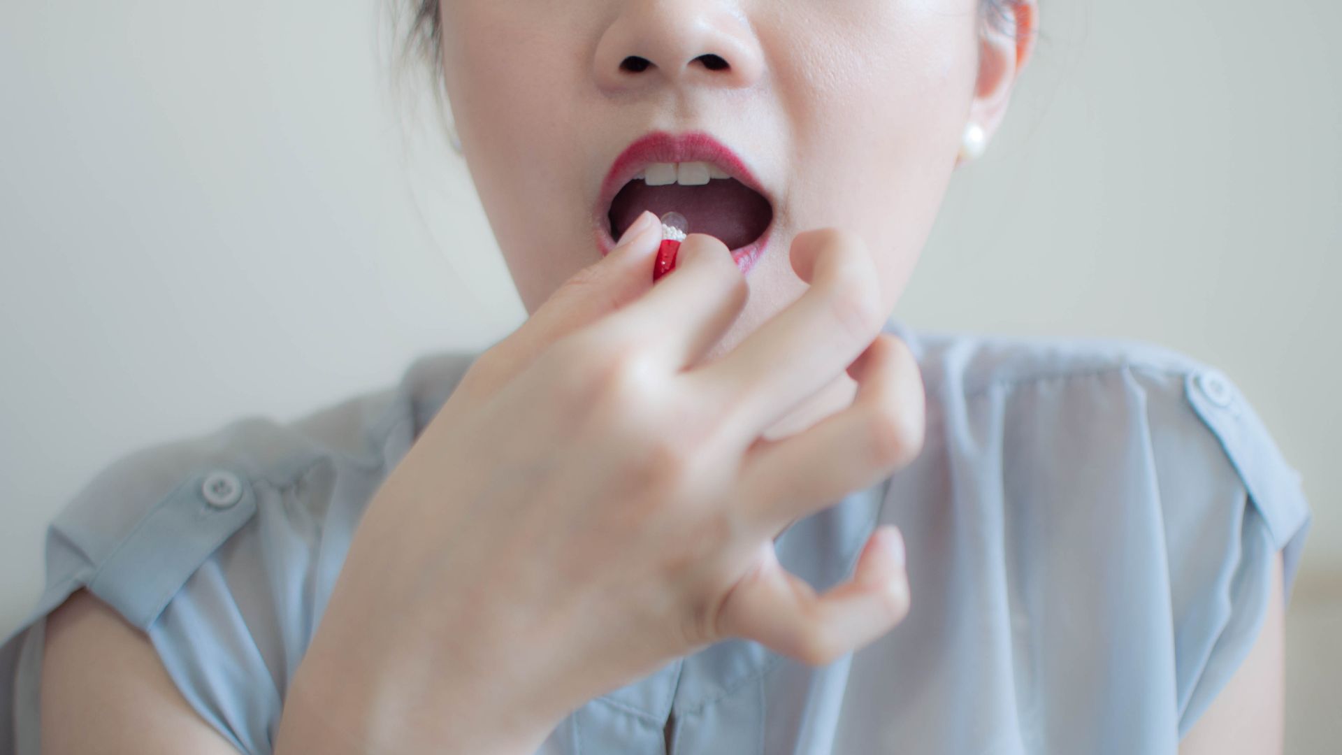 Photo of women swallowing a red and white pill