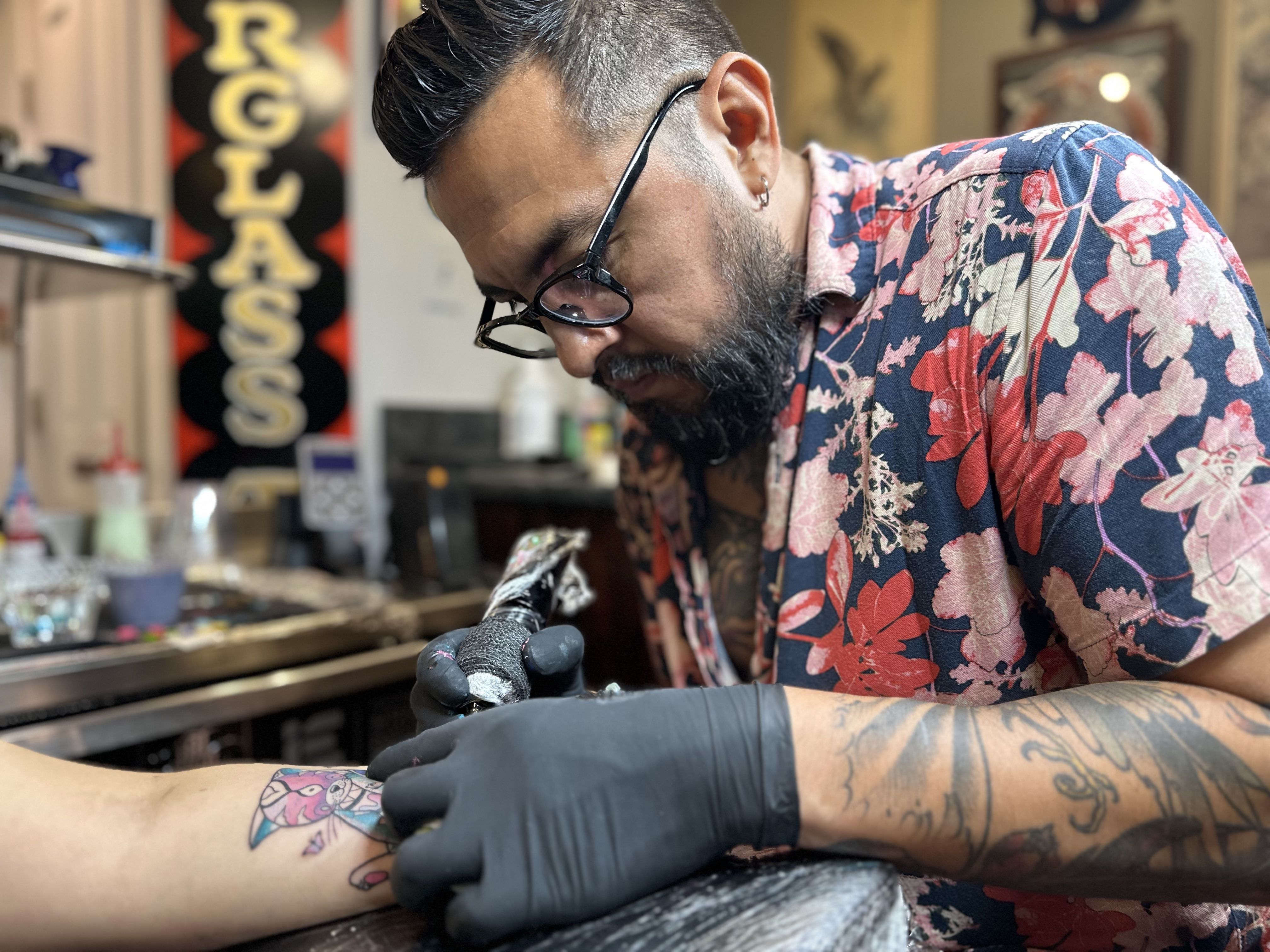 Israel Guerra Romero, AKA Spaik, tattoos a colorful cat spirit guide on a patron's forearm as a reminder of her Latin American roots.