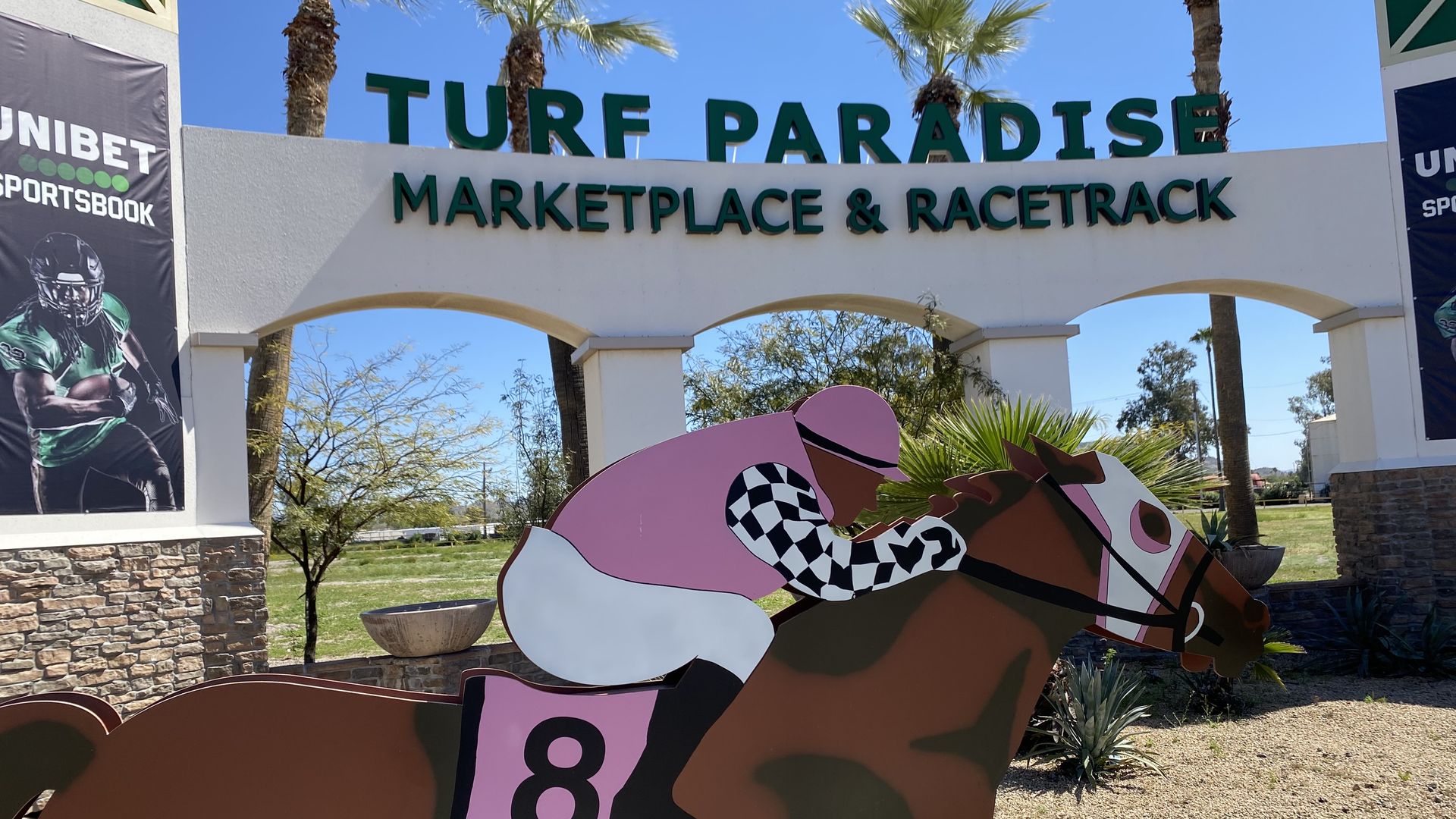 A cut-out figure of a jockey on a horse in front of a sign that reads Turf Paradise marketplace and racetrack.