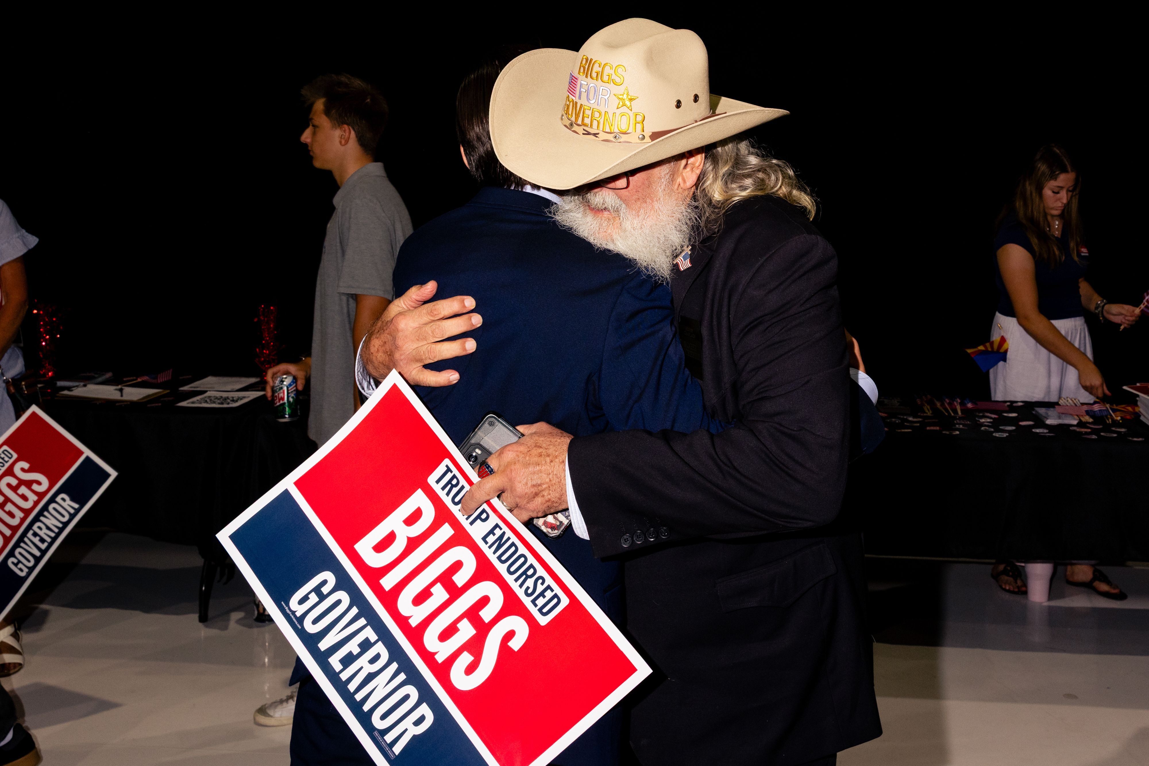 Andy Biggs' supporters embrace while holding "BIGGS GOVERNOR" sign at a victory party for his Arizona gubernatorial nomination.