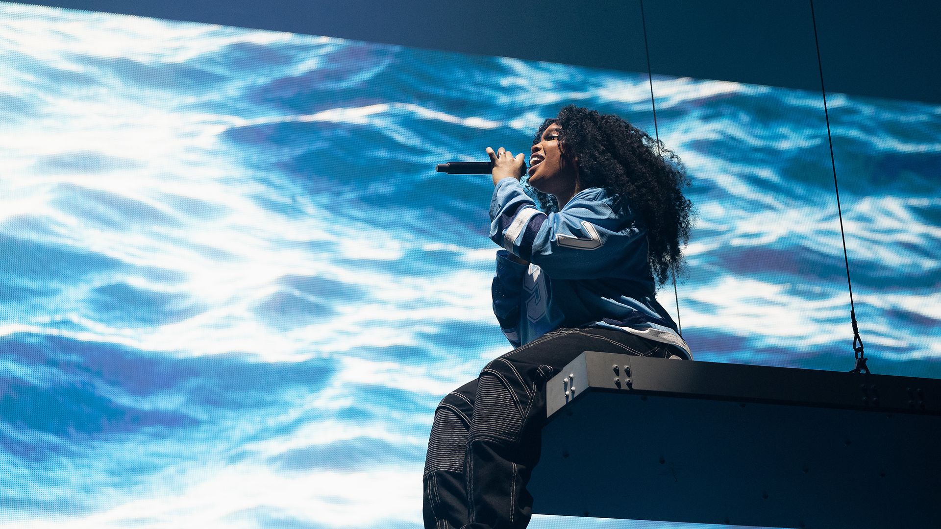 Photo of a woman on a stage, holding a microphone with a water projection.