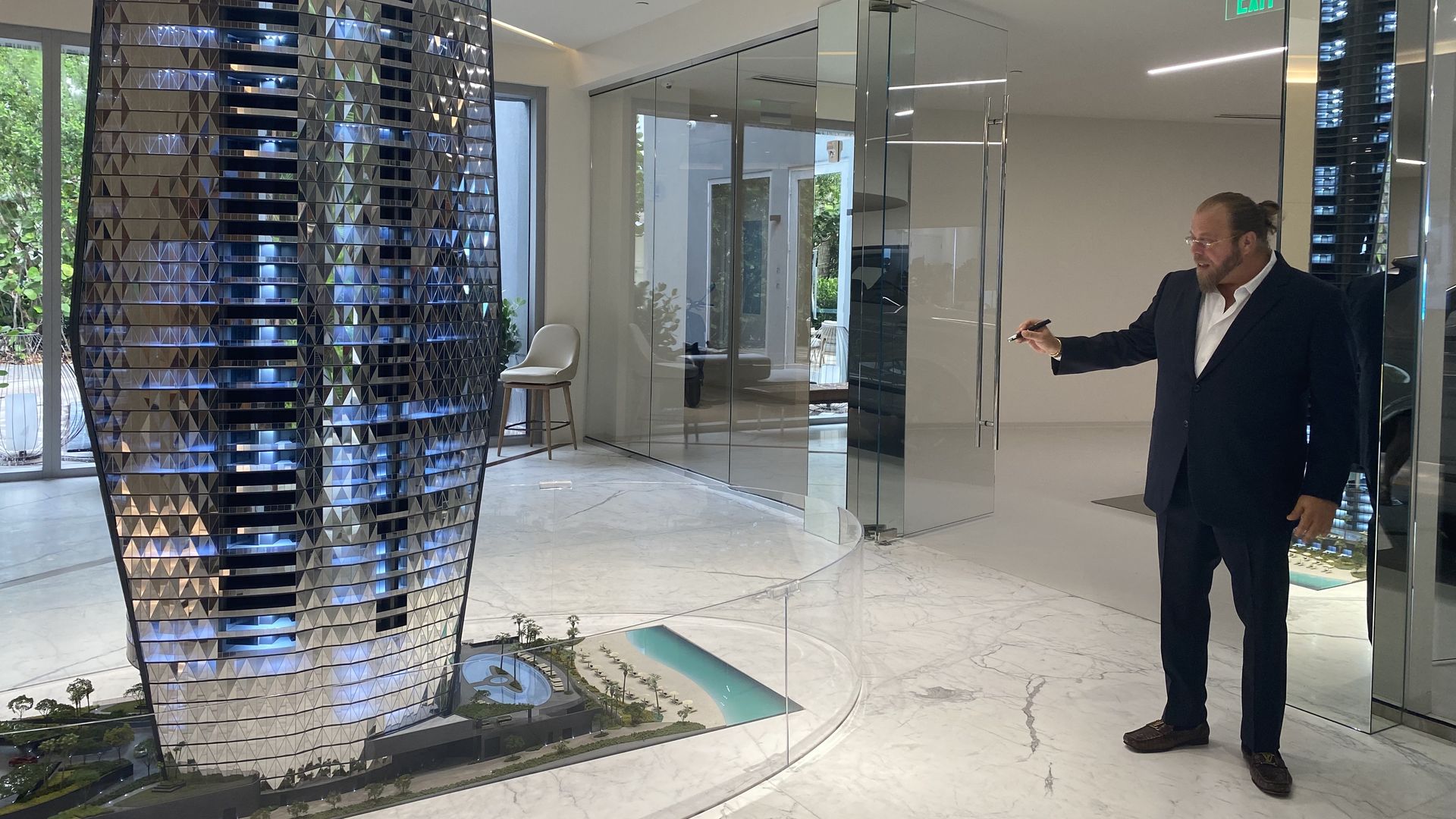 Gil Dezer wears a suit and points a laser pointer at a model of a glittering condominium tower.