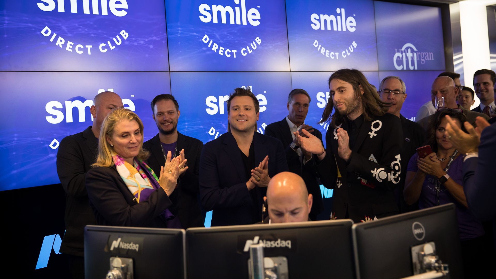 People in black shirts applaud in front of purple TV screens