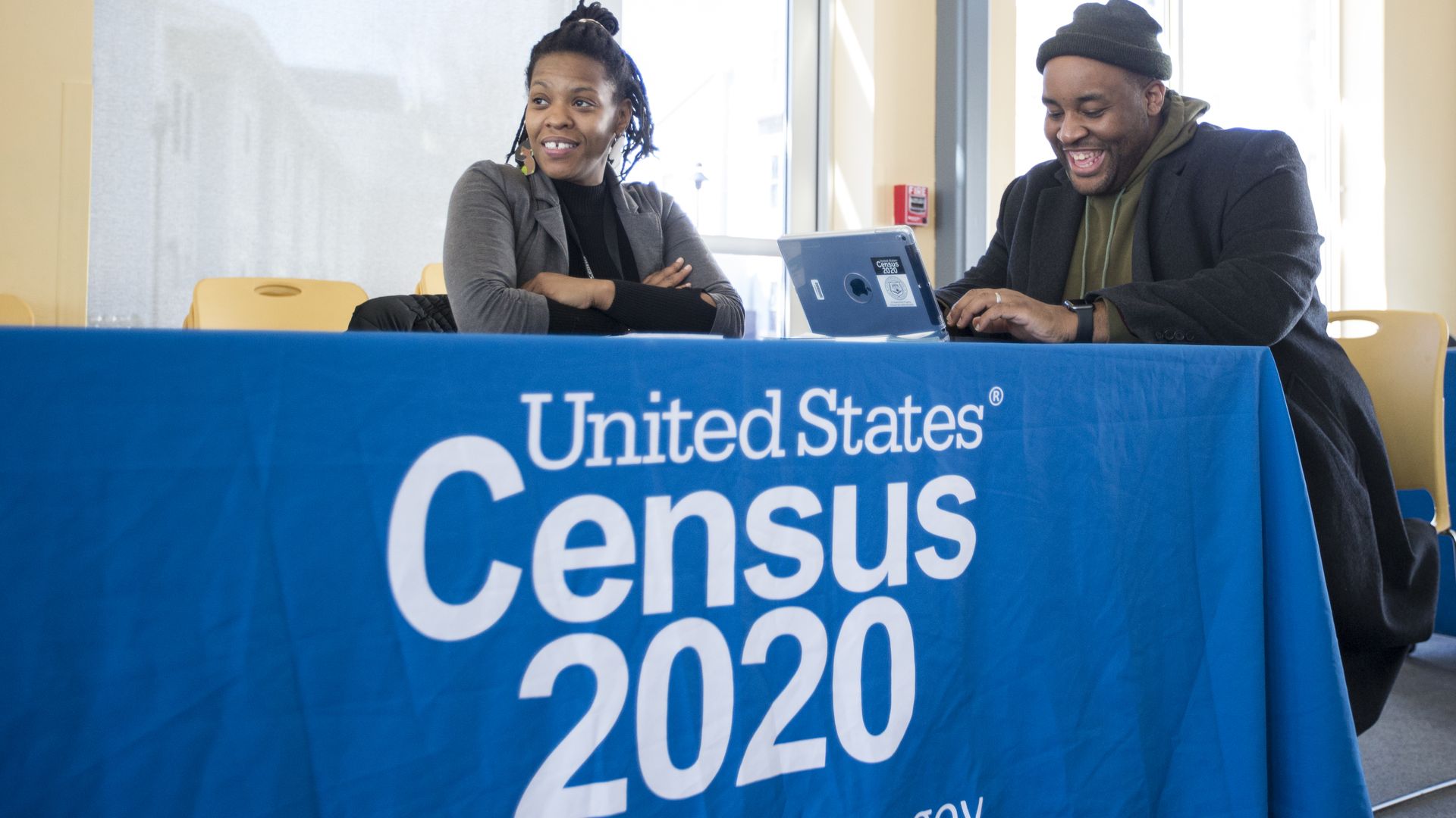 In this image, a man and a woman sit at a table that reads "Census 2020"