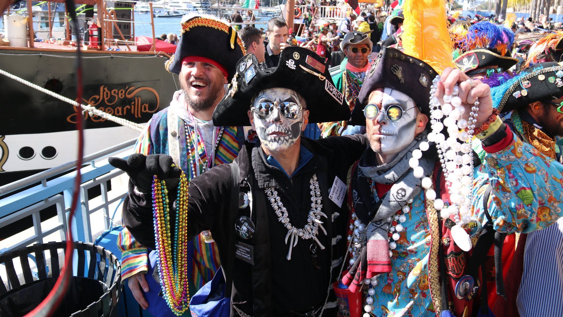 Two men dressed as pirates hold up multi-colored plastic parade beads.
