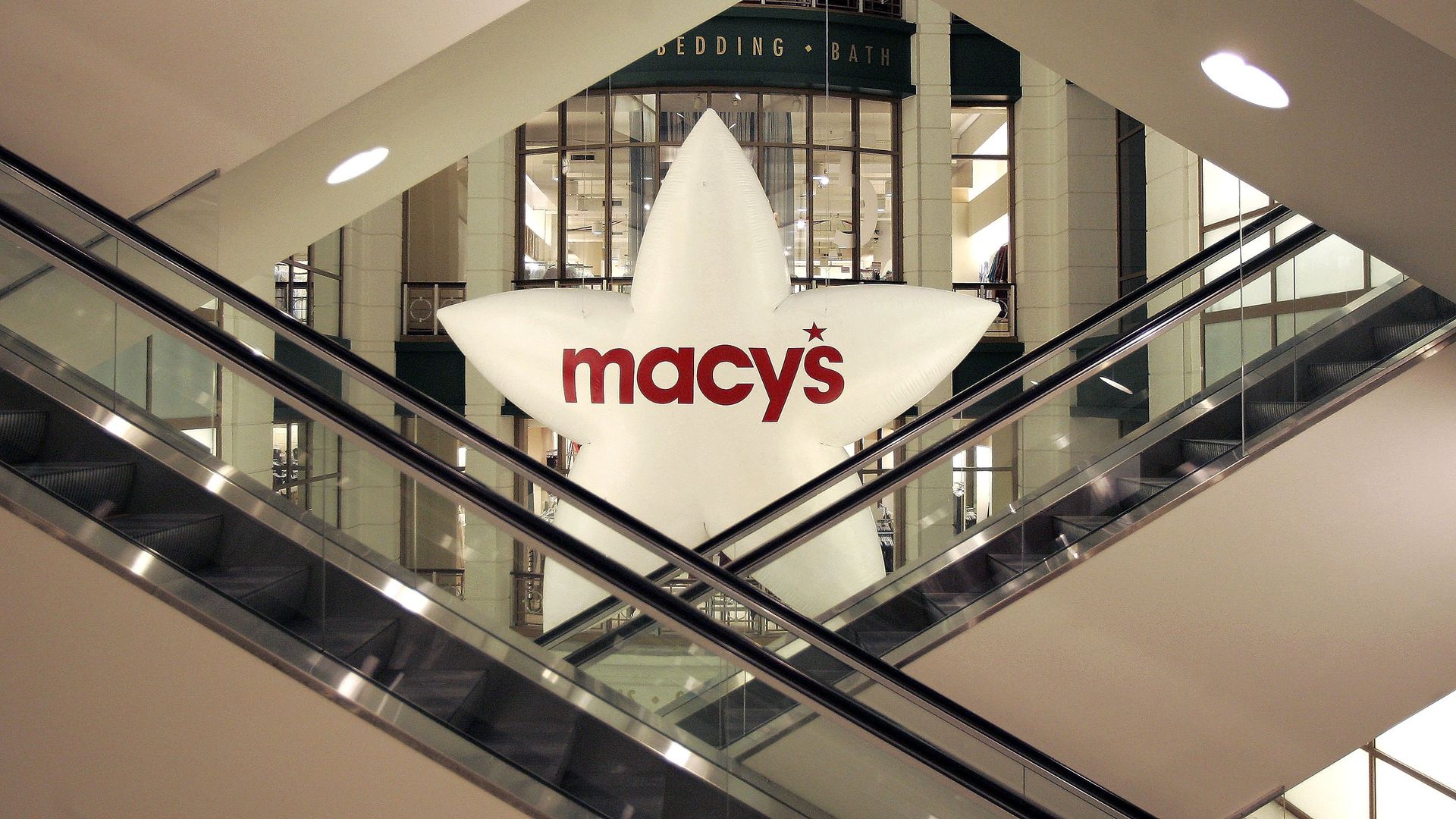 An inflatable white balloon shaped like a star that reads Macy's hanging behind escalators.