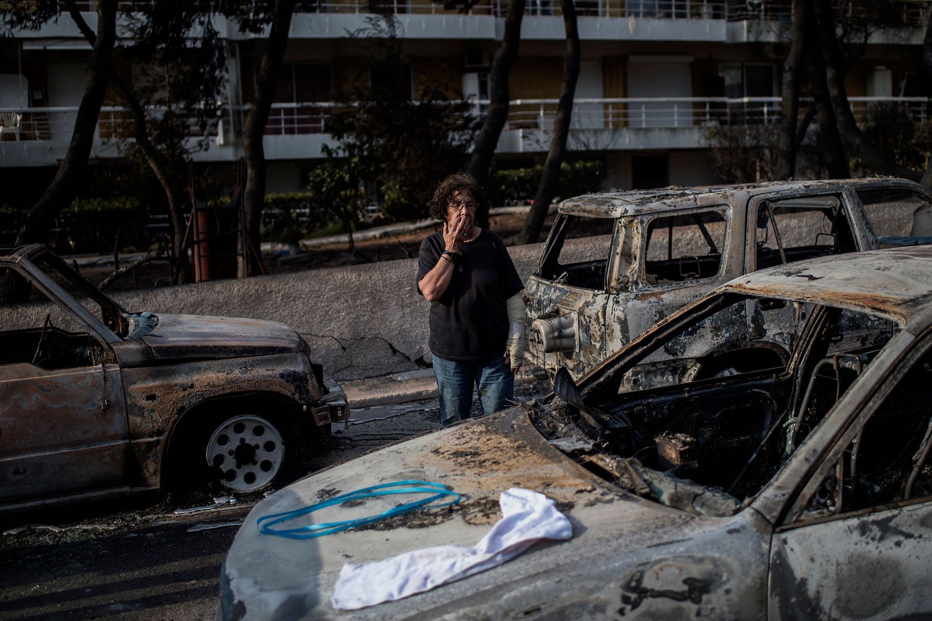 A woman with a cast stands among cars burnt following a wildfire at the village of Mati, near Athens, on July 24, 2018.