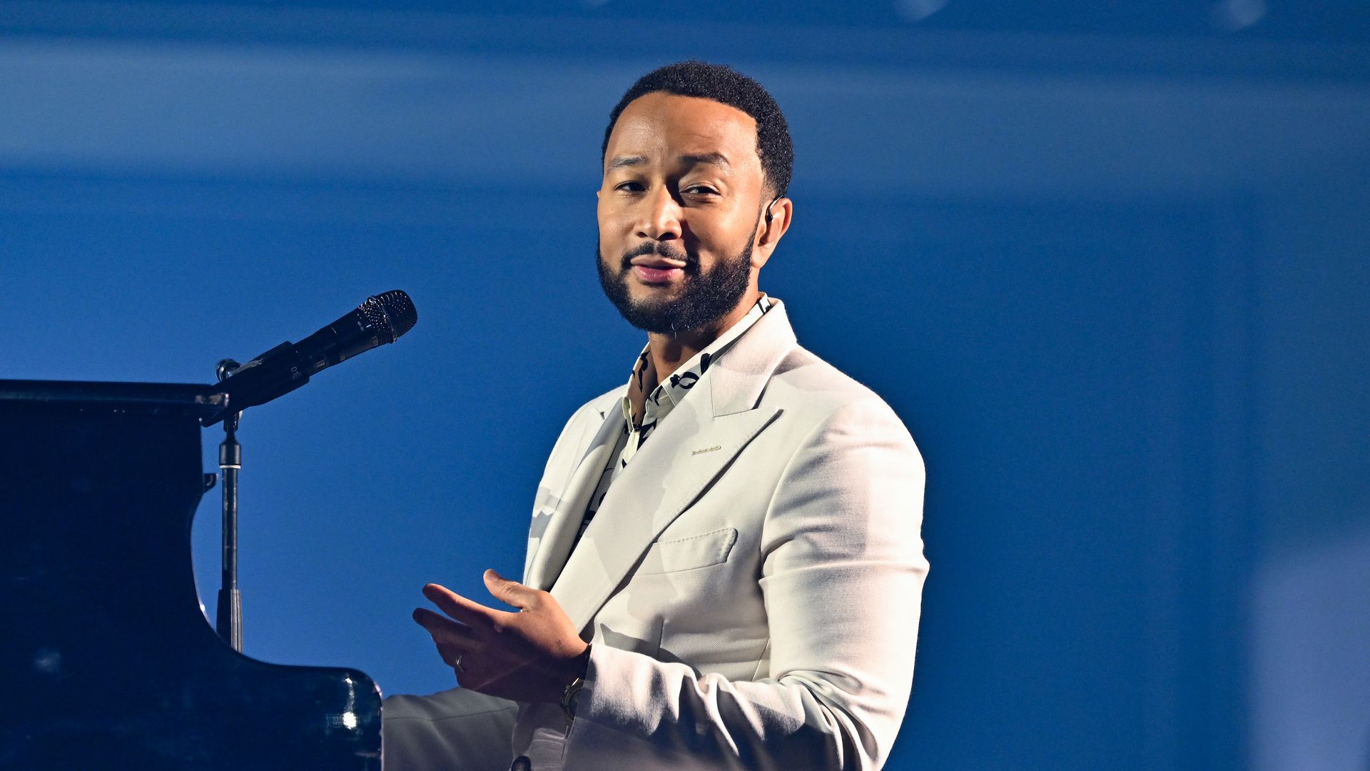 John Legend sits at a piano on stage. 