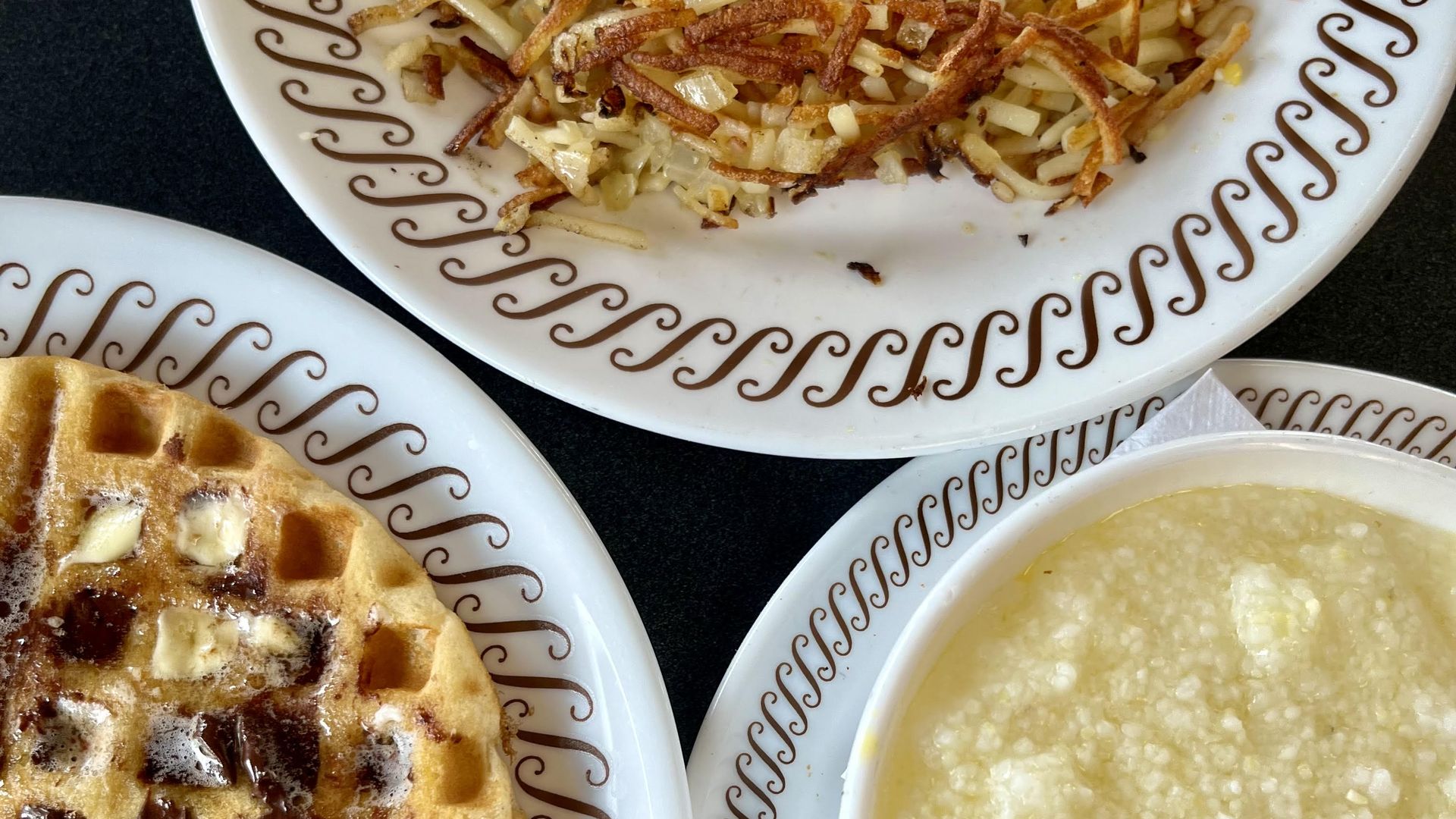 A waffle with butter and chocolate, a bowl of cheese grits and a plate of hash browns from Waffle House.